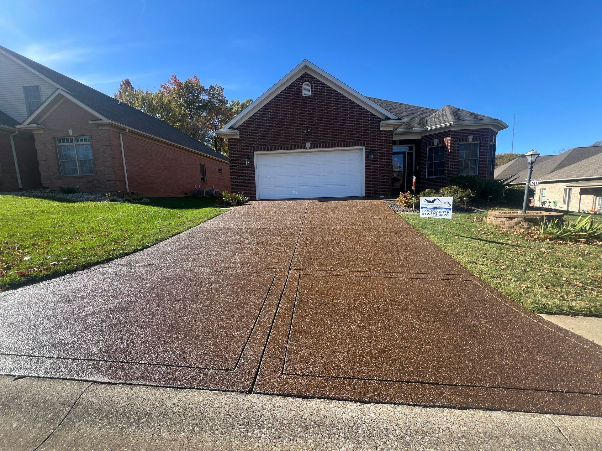 Driveway leading to a brick house on a sunny day. The driveway is a dark aggregate.