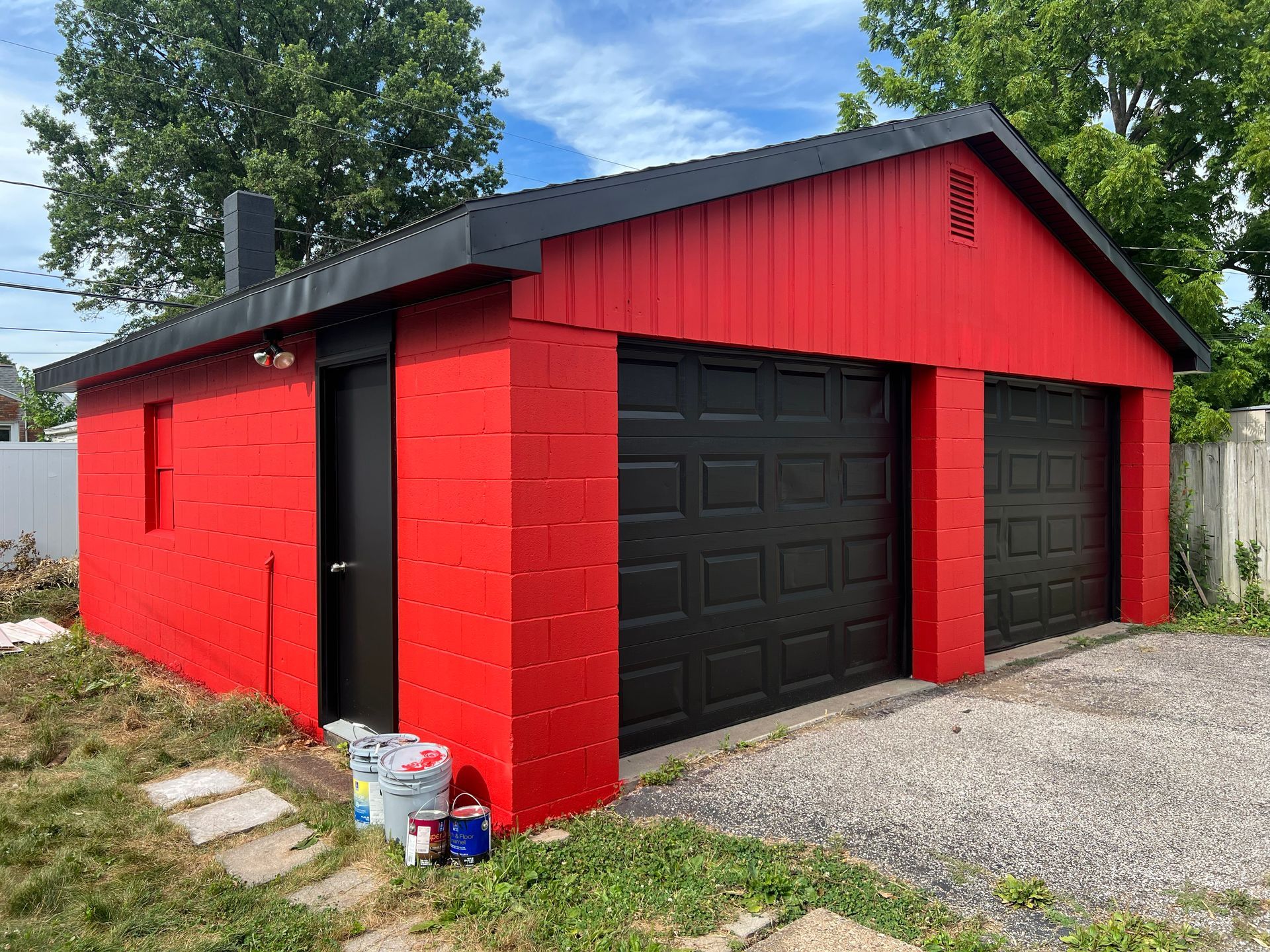 Red and black garage with two garage doors and a side door, grass and driveway.
