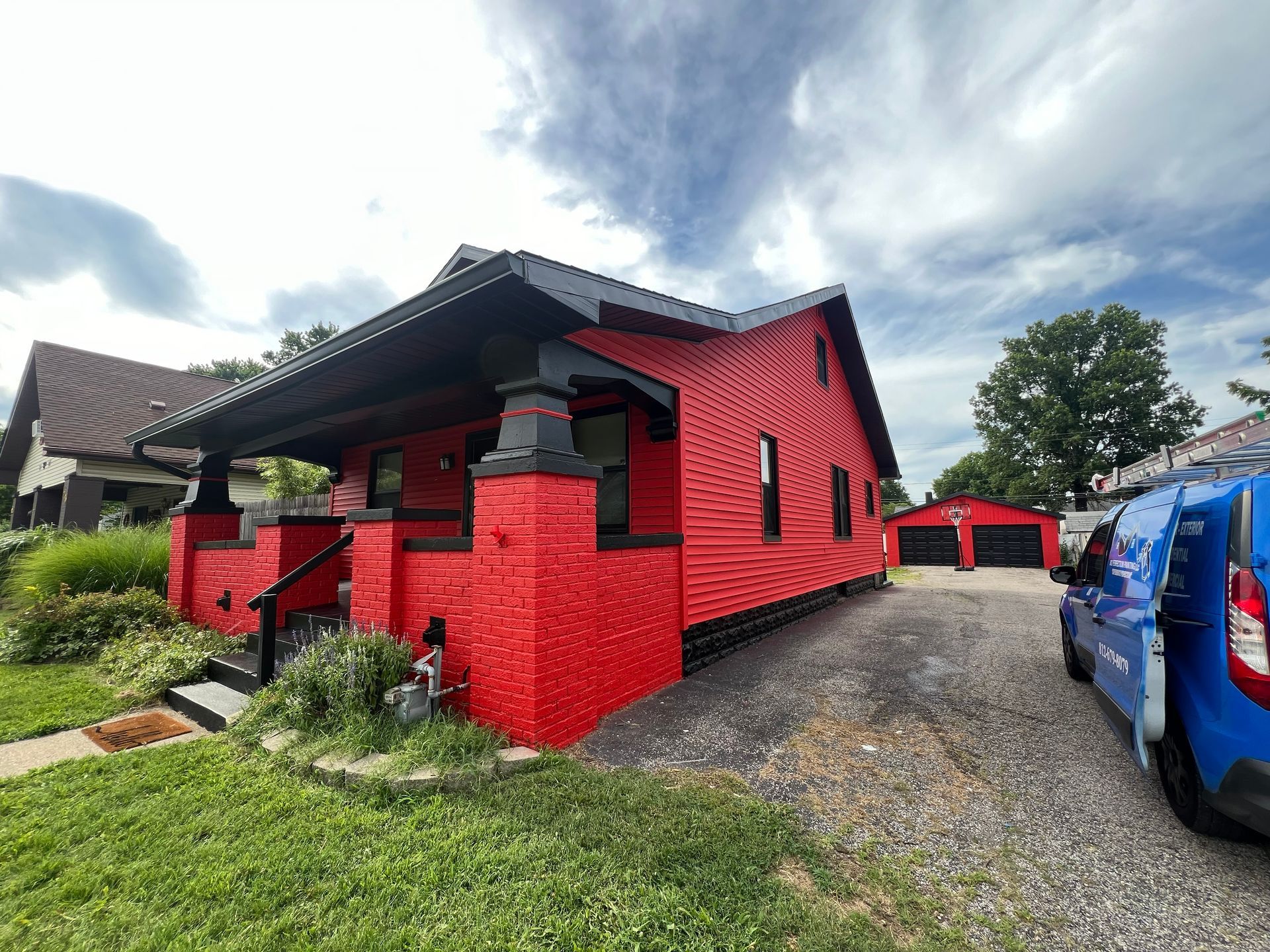 Red house with black trim, a blue van parked in front. Overcast sky.