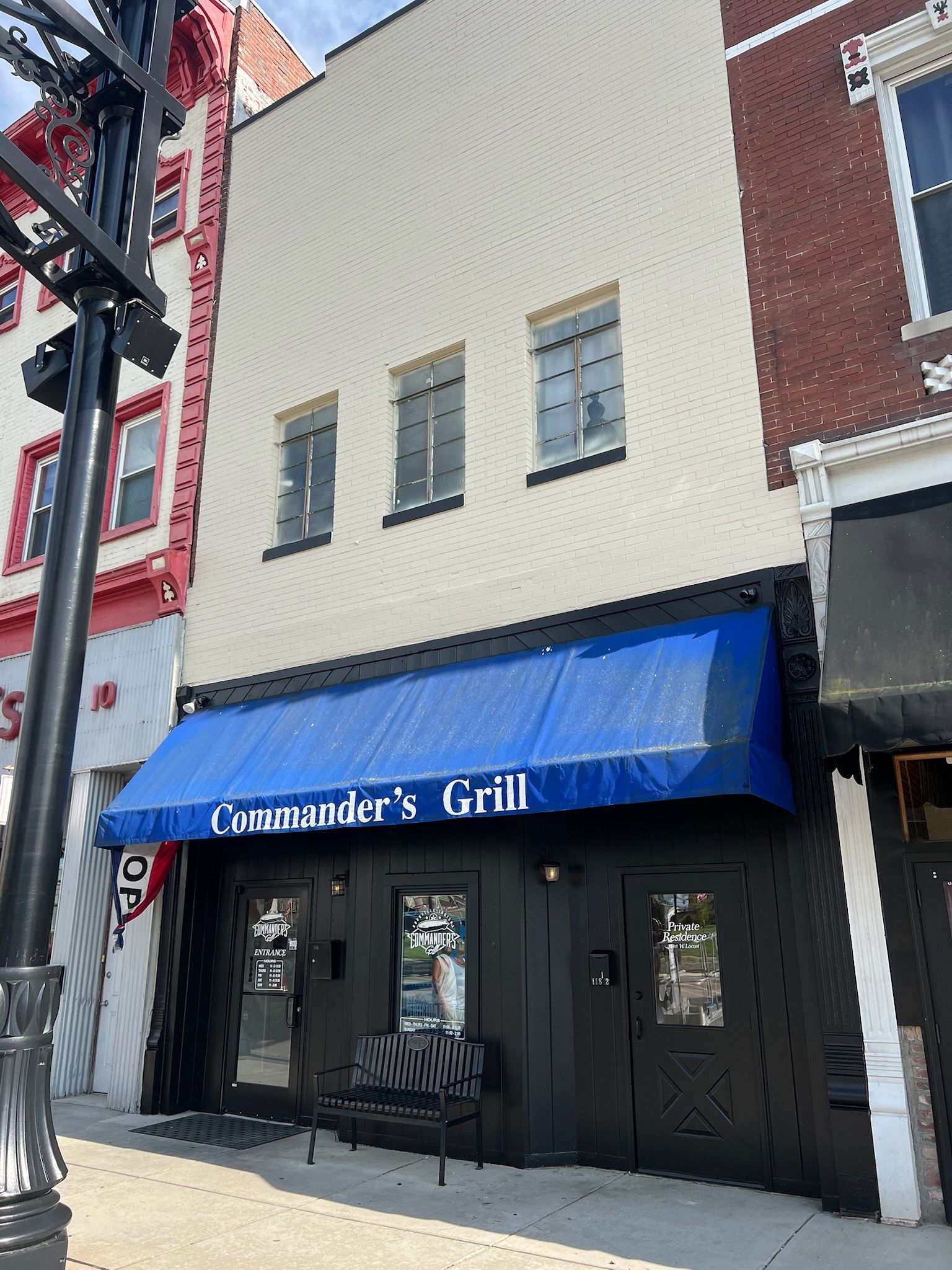 Exterior of Commander's Grill restaurant with a blue awning and three windows.