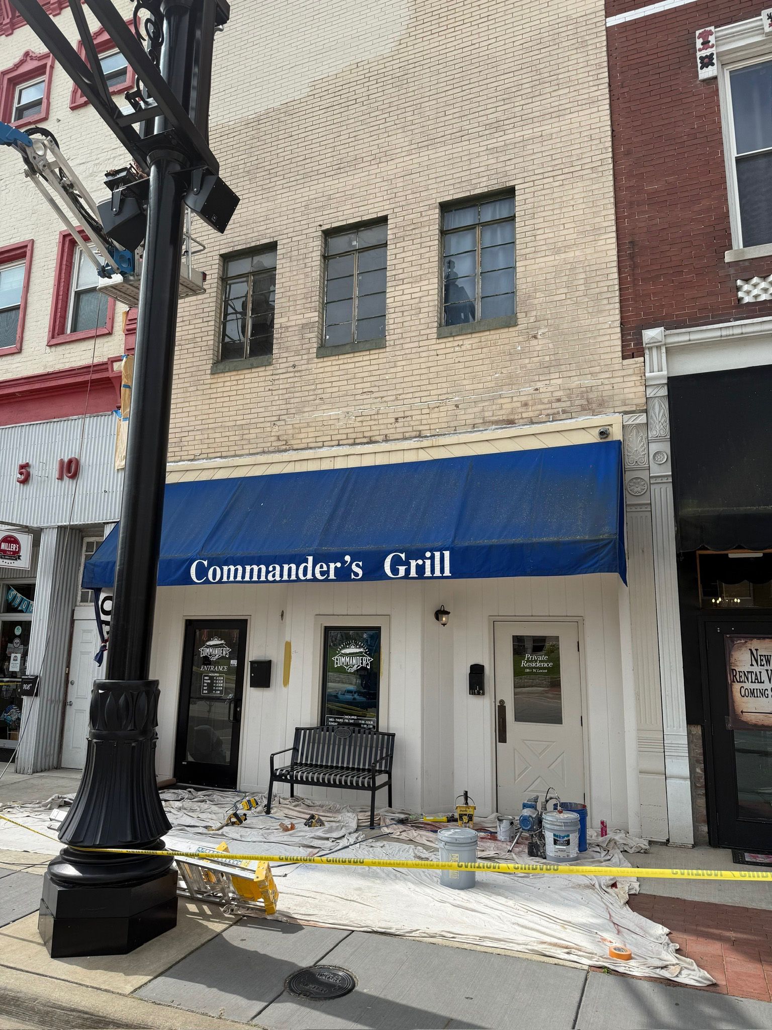 Commander's Grill storefront with blue awning. Brick building with damage to sidewalk. Yellow caution tape present.