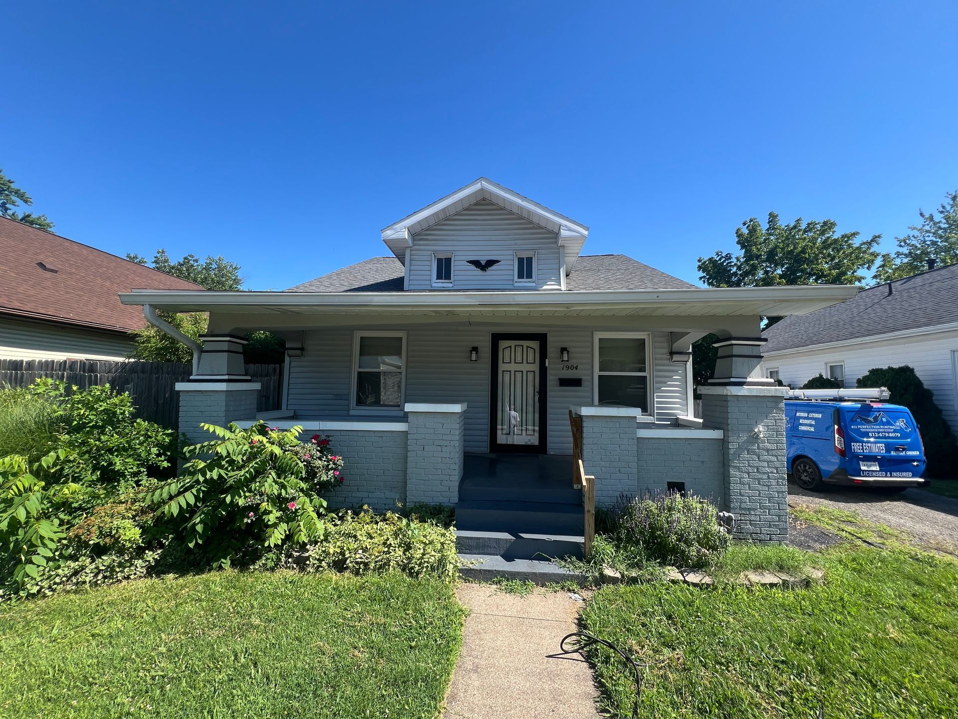 Blue house with porch, gray pillars, green lawn, blue sky.