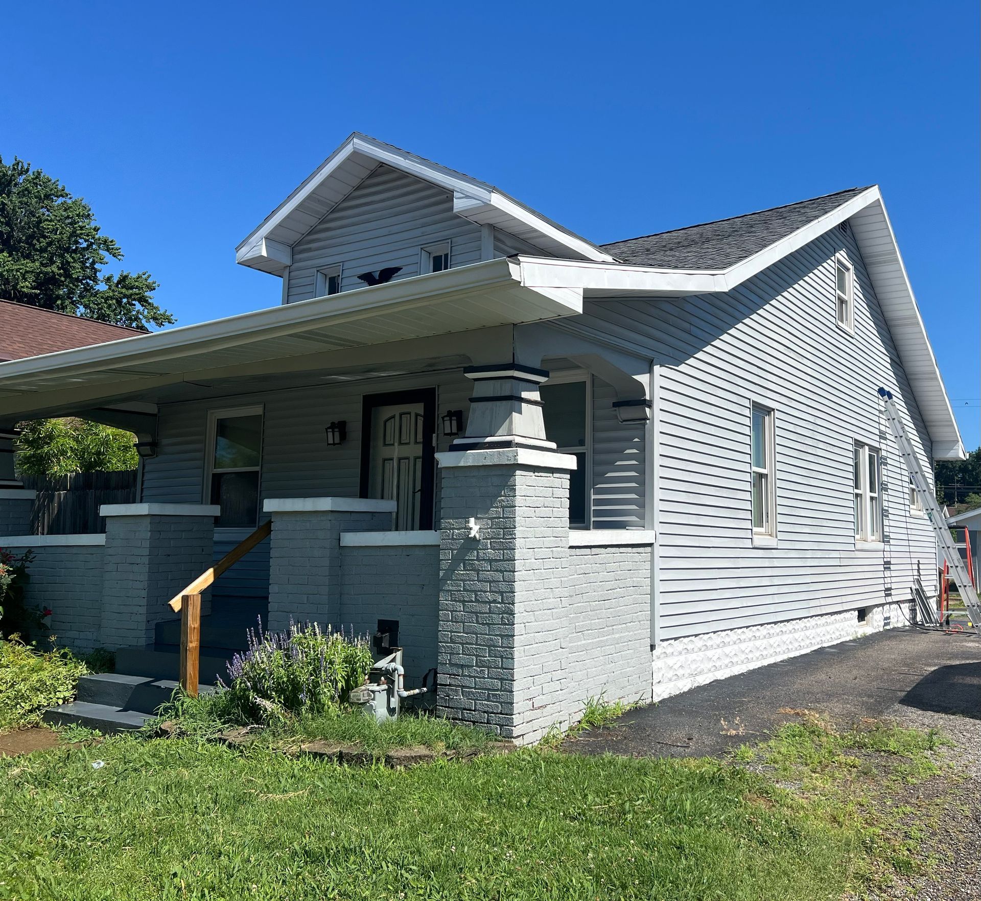 A gray house with white trim and a porch under a clear blue sky.