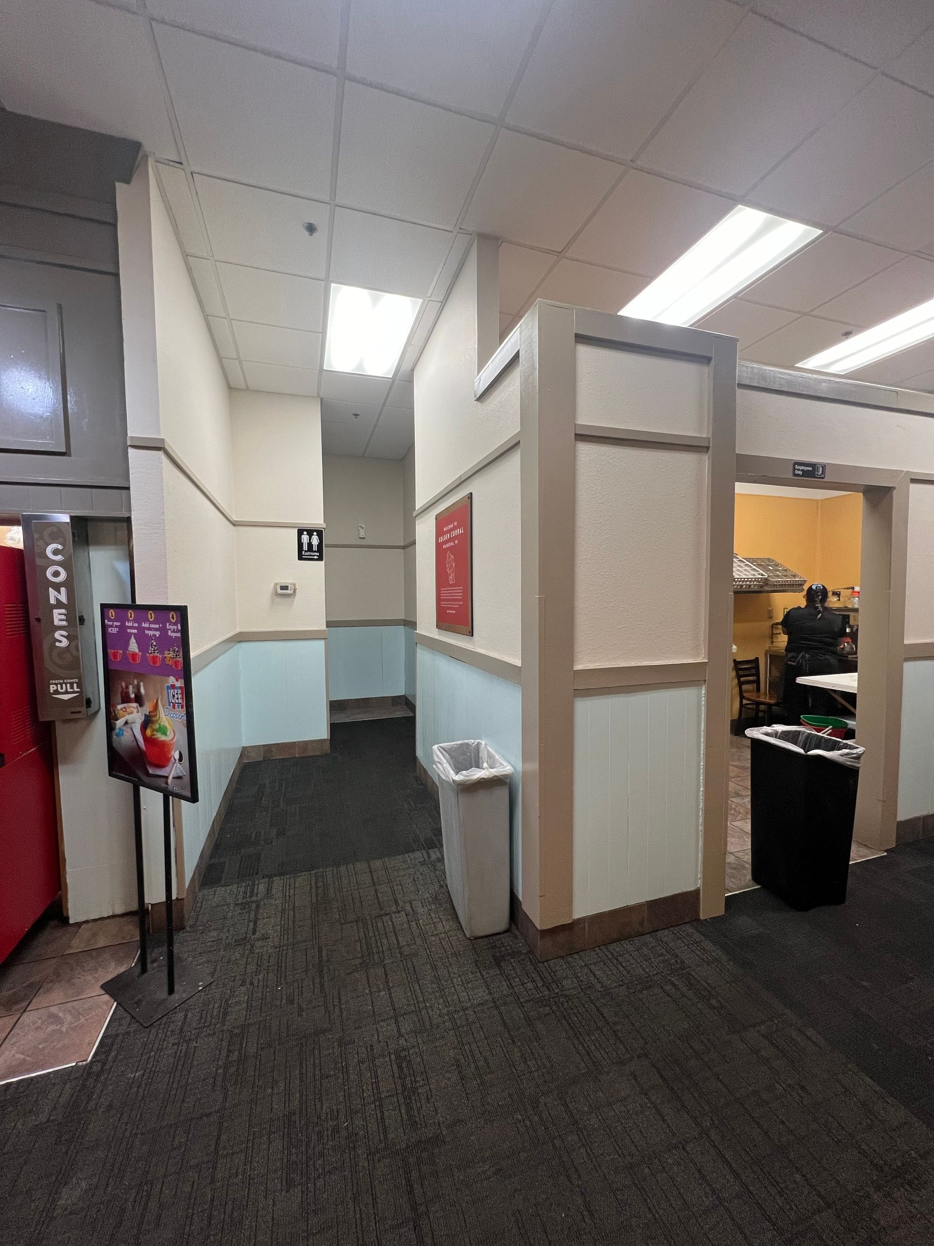 Hallway with carpet and walls, a stand with a sign, and a doorway to an office.