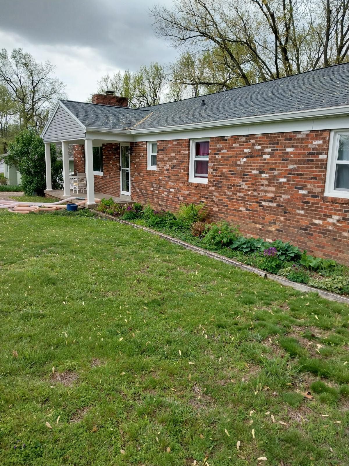 Red brick house with a green lawn and a small flower bed along the front.