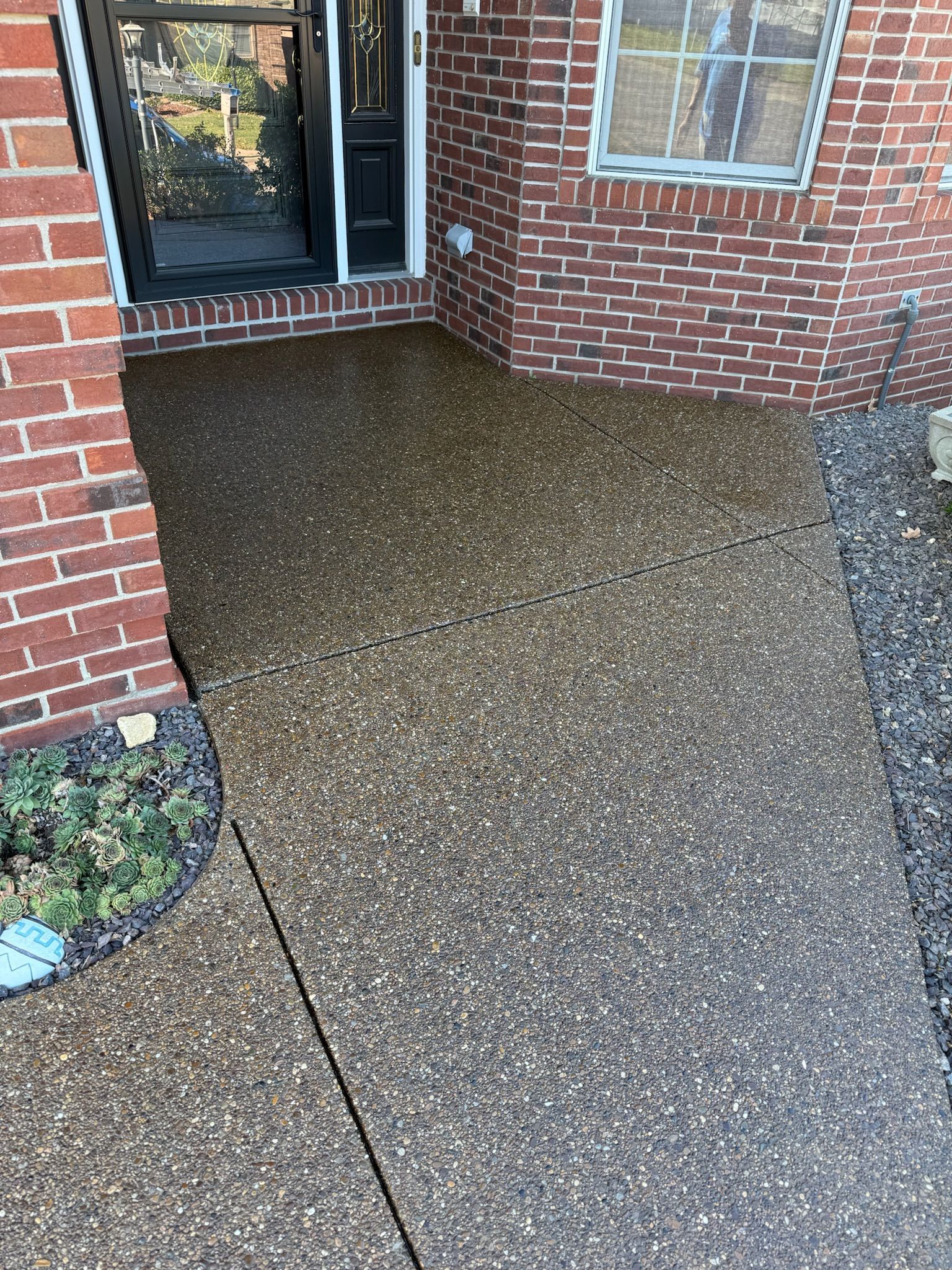 Brick porch with speckled concrete, leading to a glass door; red brick wall on the side.