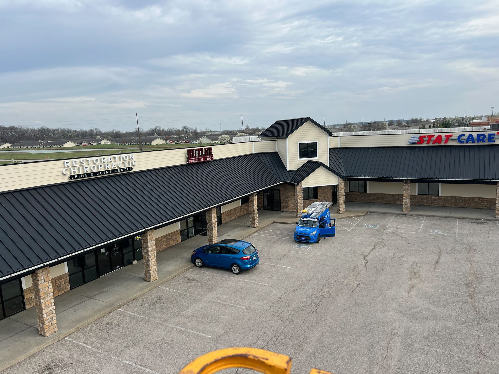 Exterior of a single-story strip mall on a cloudy day; blue cars are parked in front.