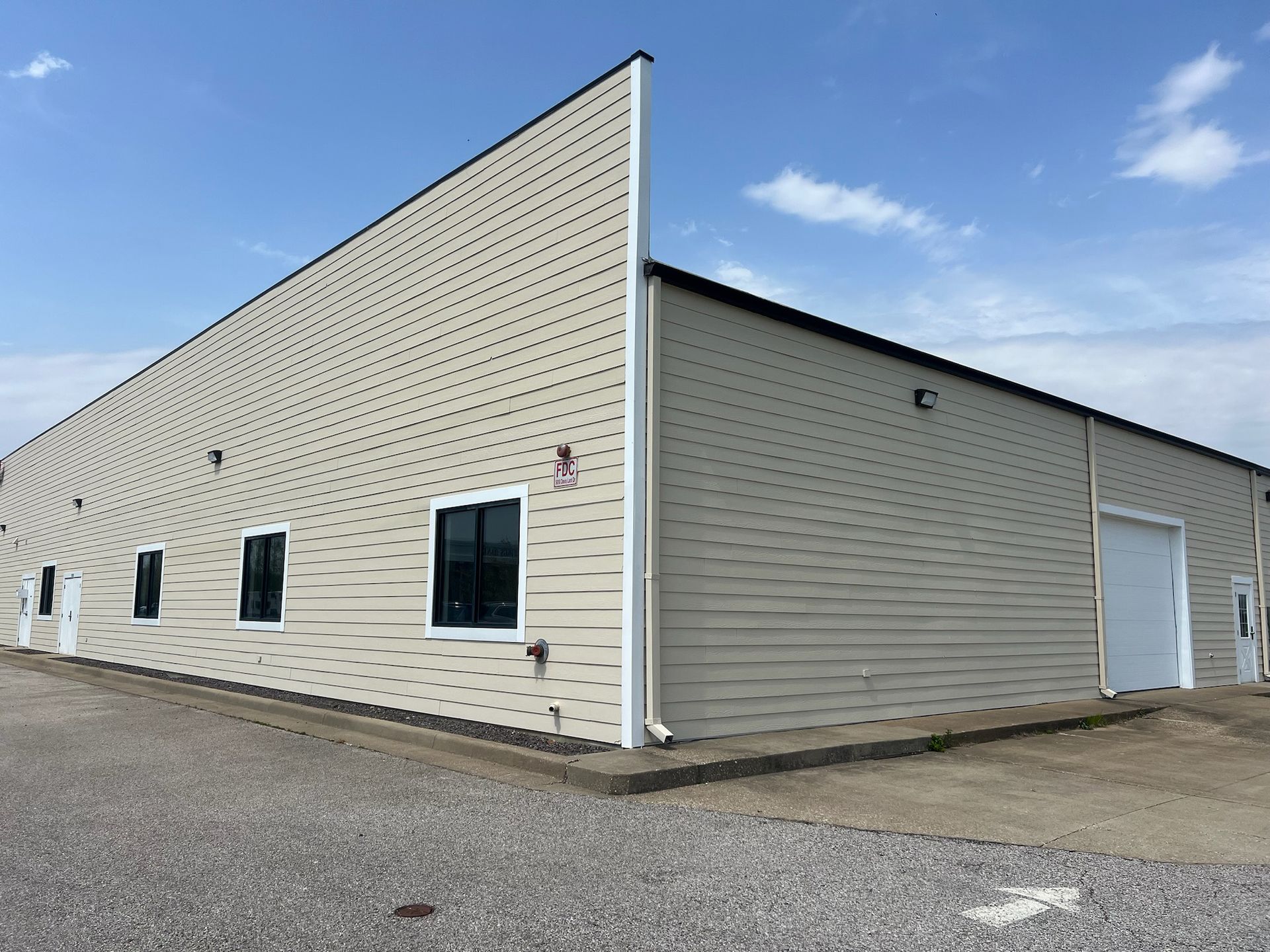 Tan industrial building with windows and a large white door against a partly cloudy sky.
