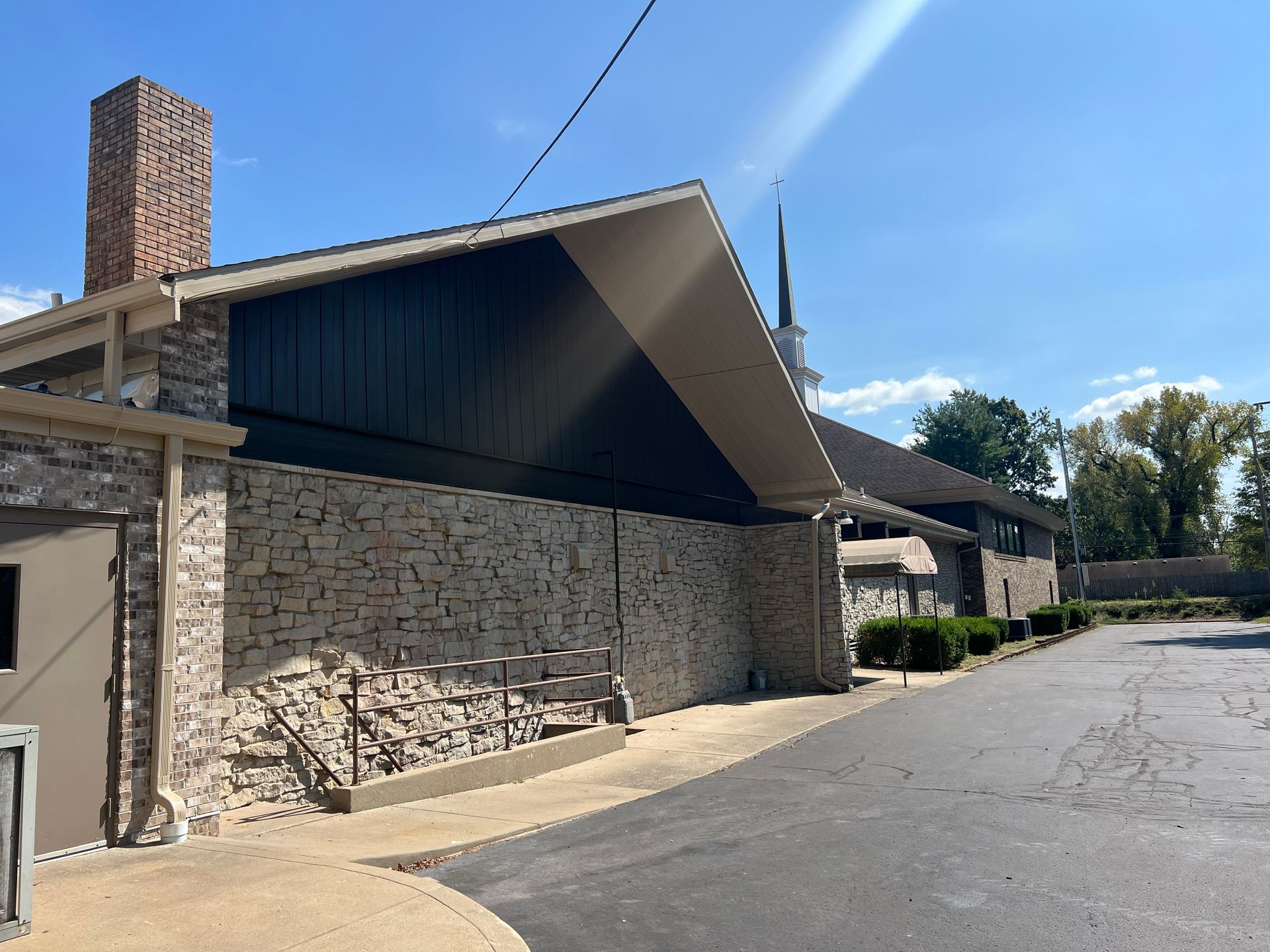 Exterior of a stone-walled building with a peaked roof and a brick chimney under a blue sky.