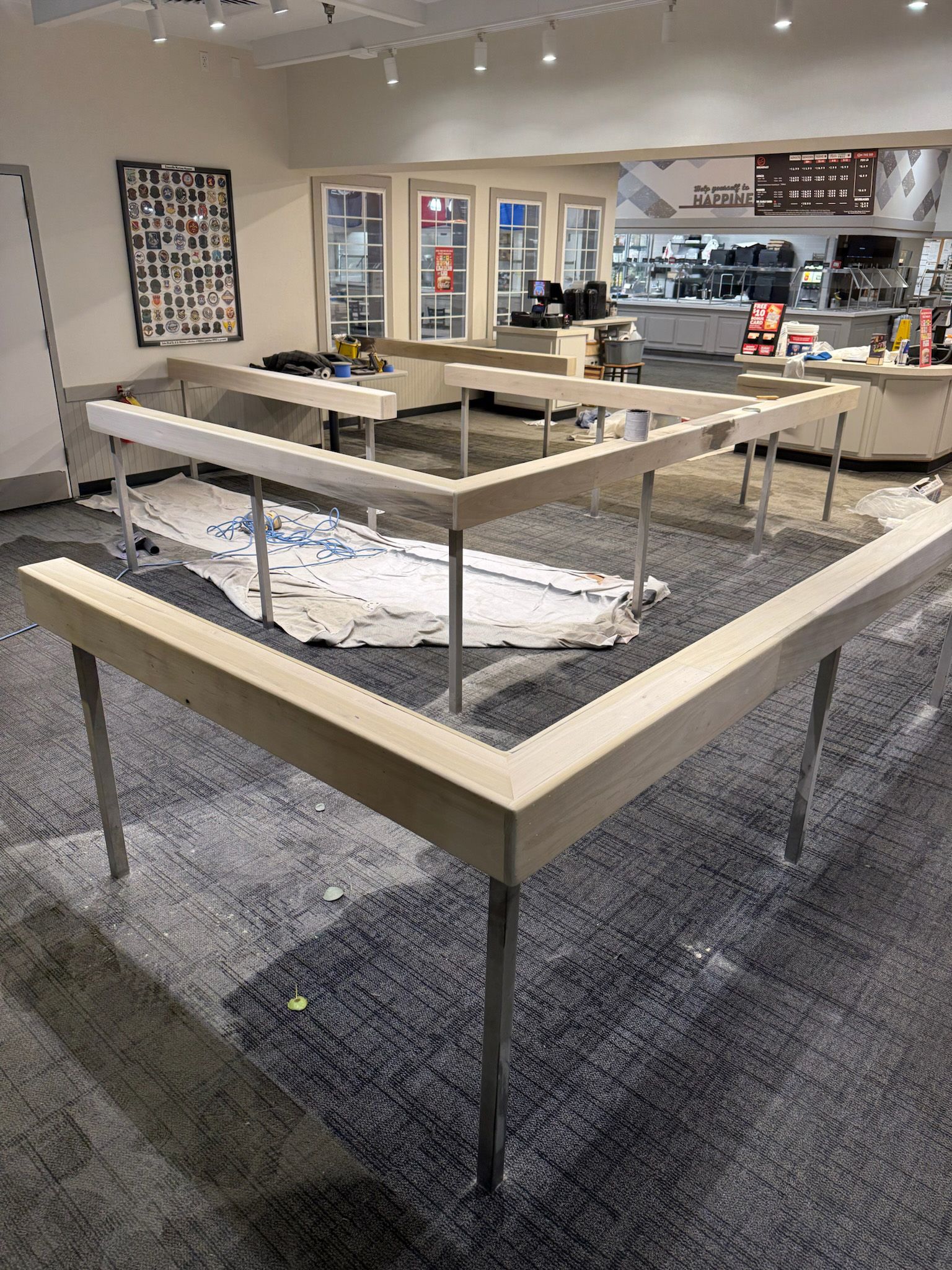Light wood display tables in a store, arranged in a large angular shape. White paper covers the floor.