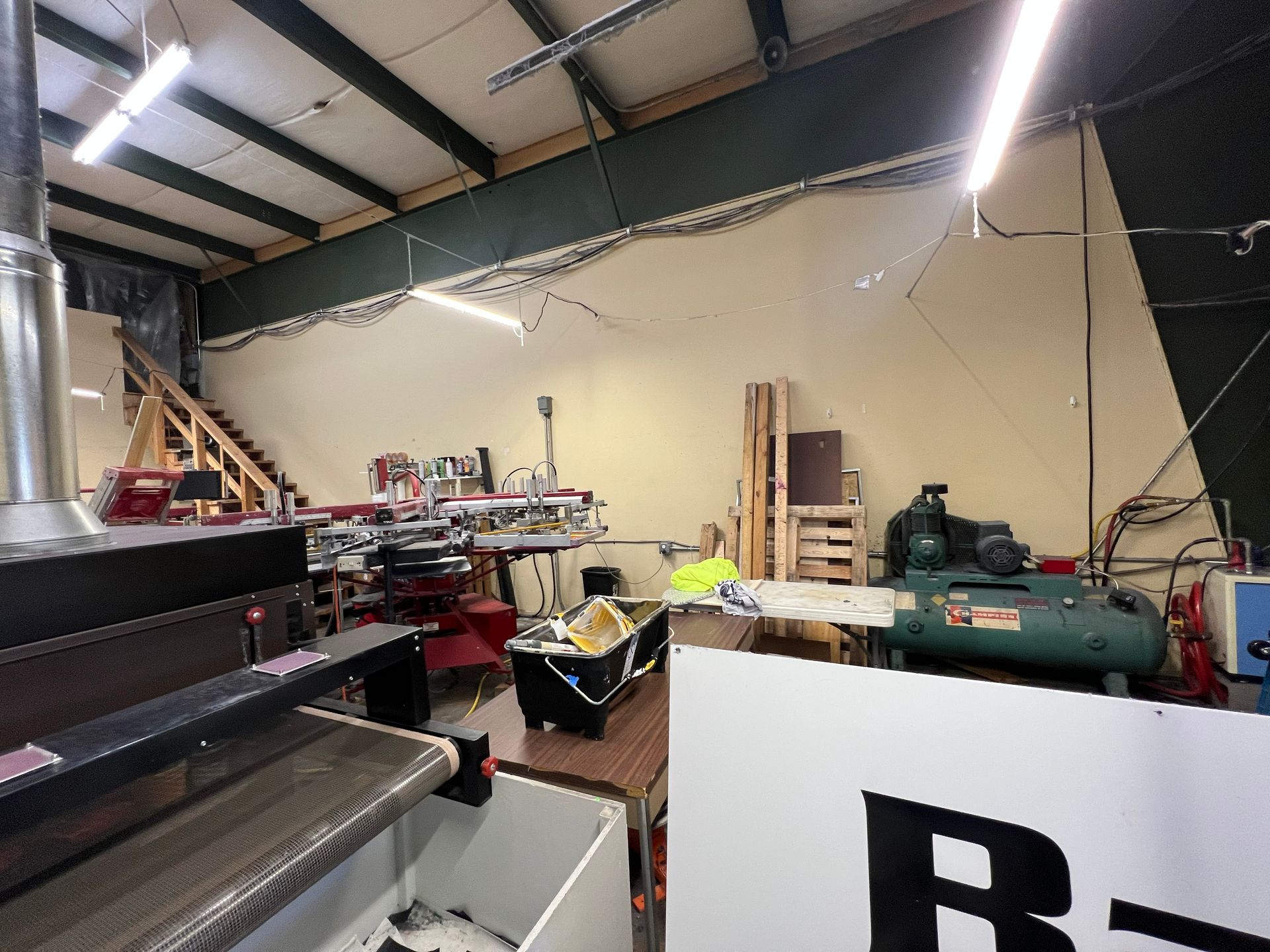 Workshop interior with machinery and tools, including an air compressor and stairs leading upward.