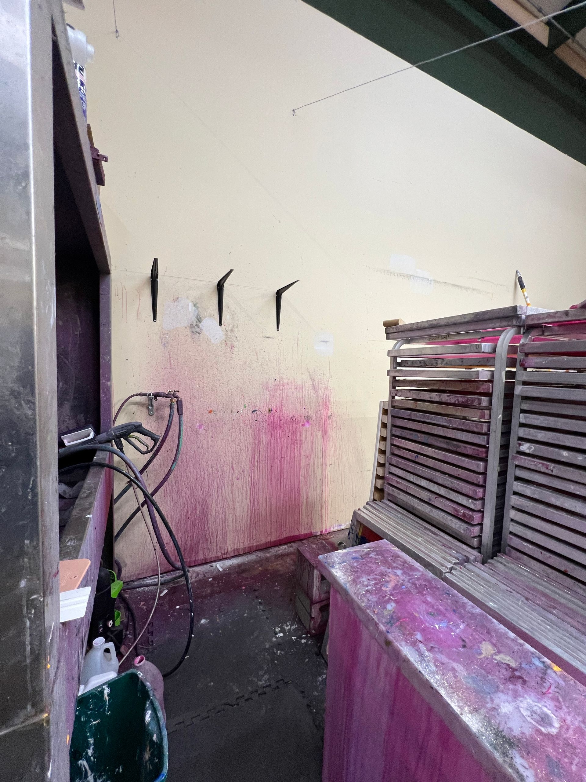Wine-stained wall and machinery in an industrial setting; four black hooks on the wall.