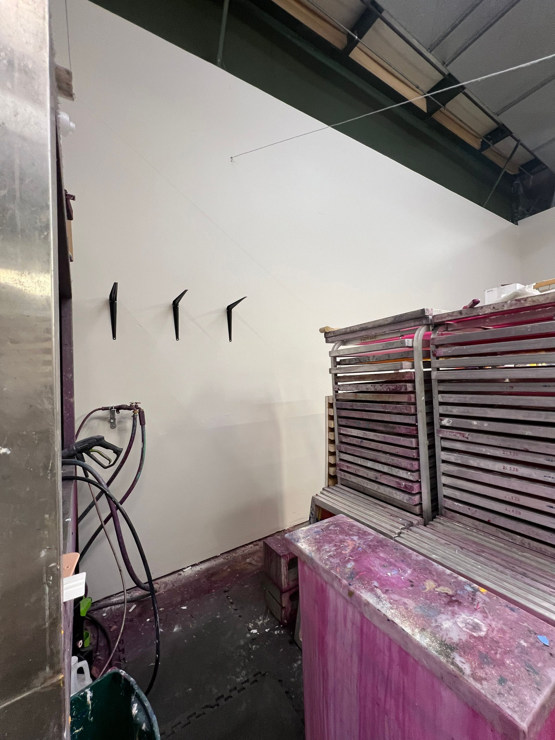 A corner of a workshop with a painted wall, hooks, and a drying rack with magenta staining.