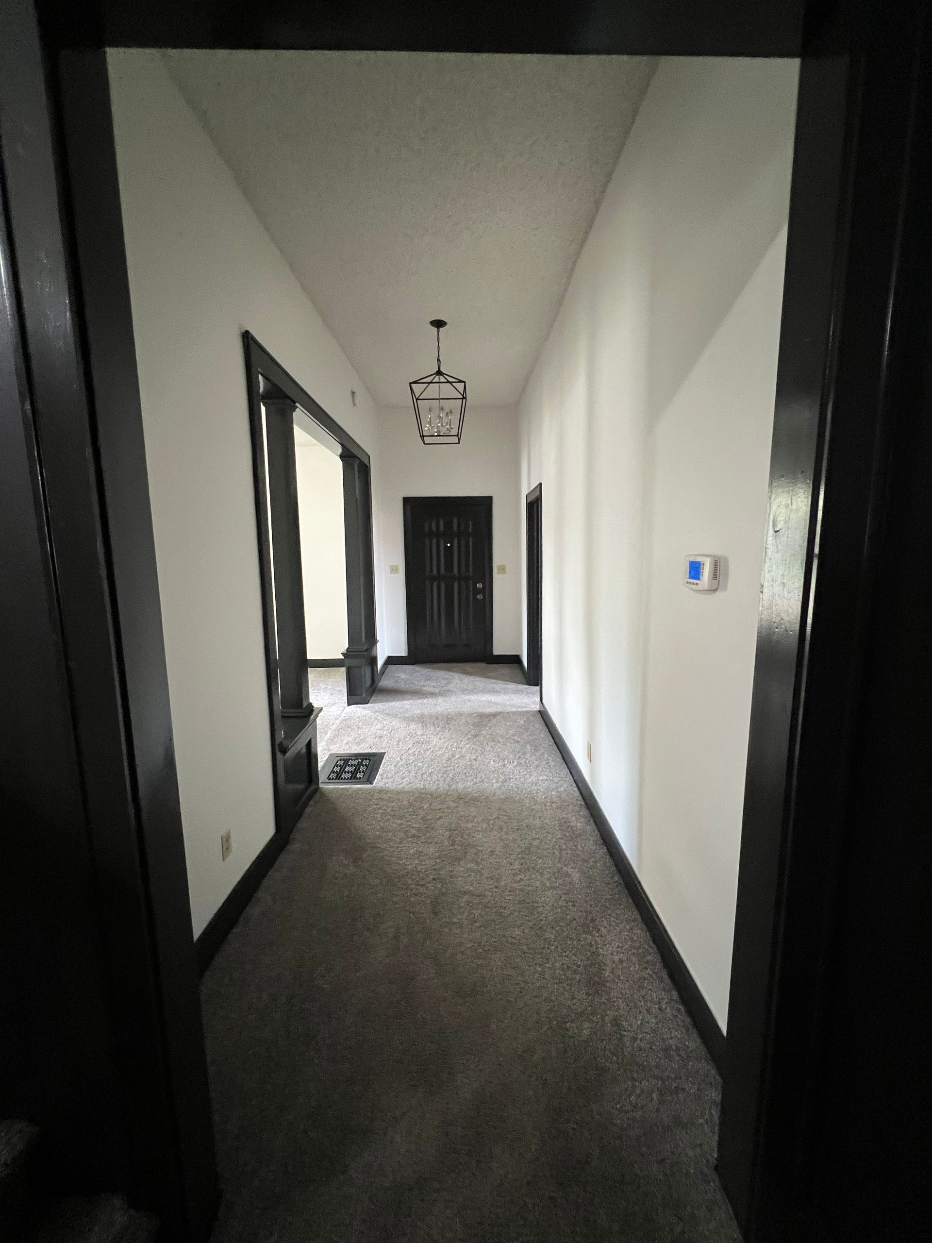 Long hallway with dark trim, white walls, gray carpet, and a black door at the end.
