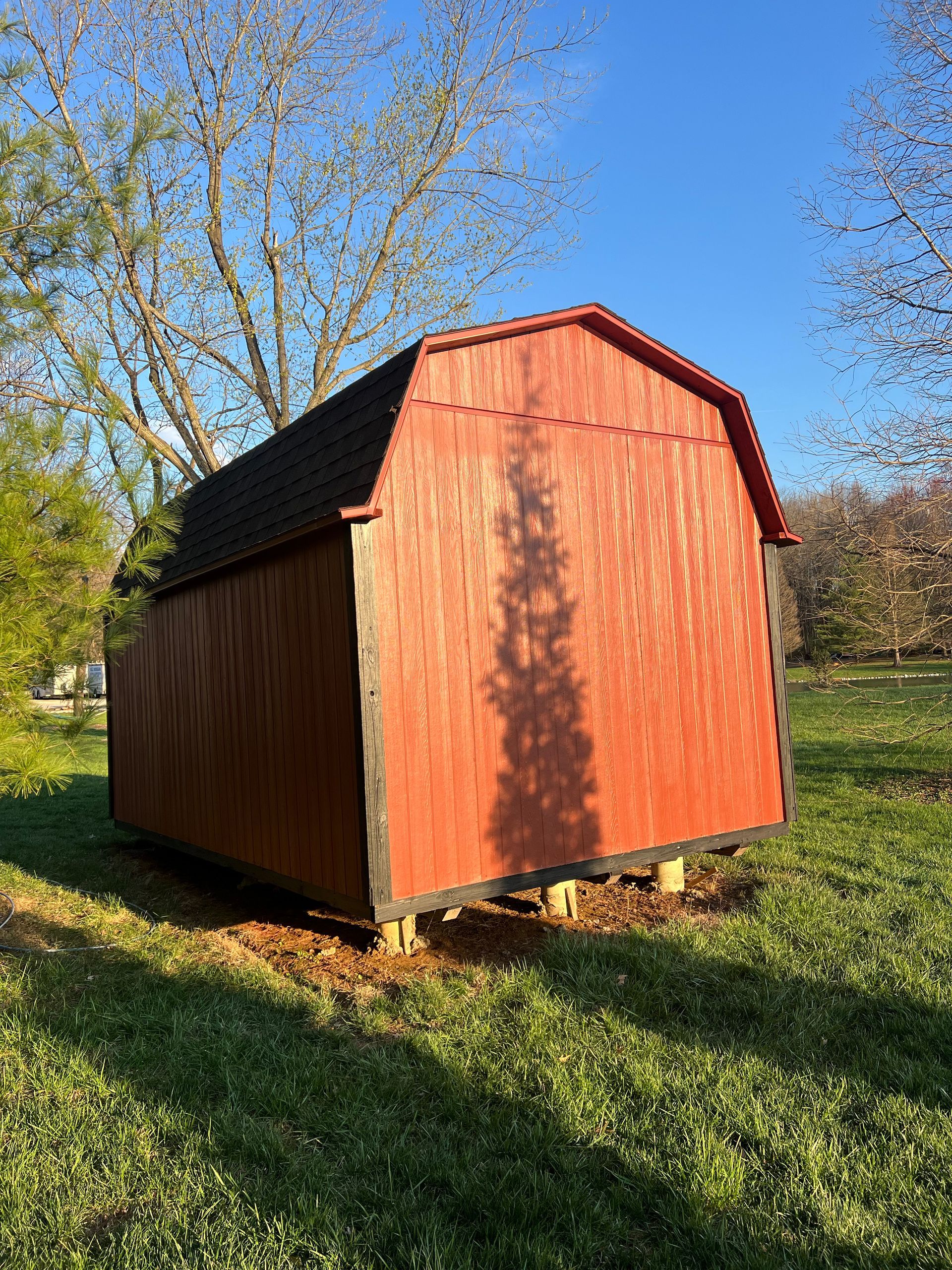 Red barn-style shed on grass in a sunny yard.