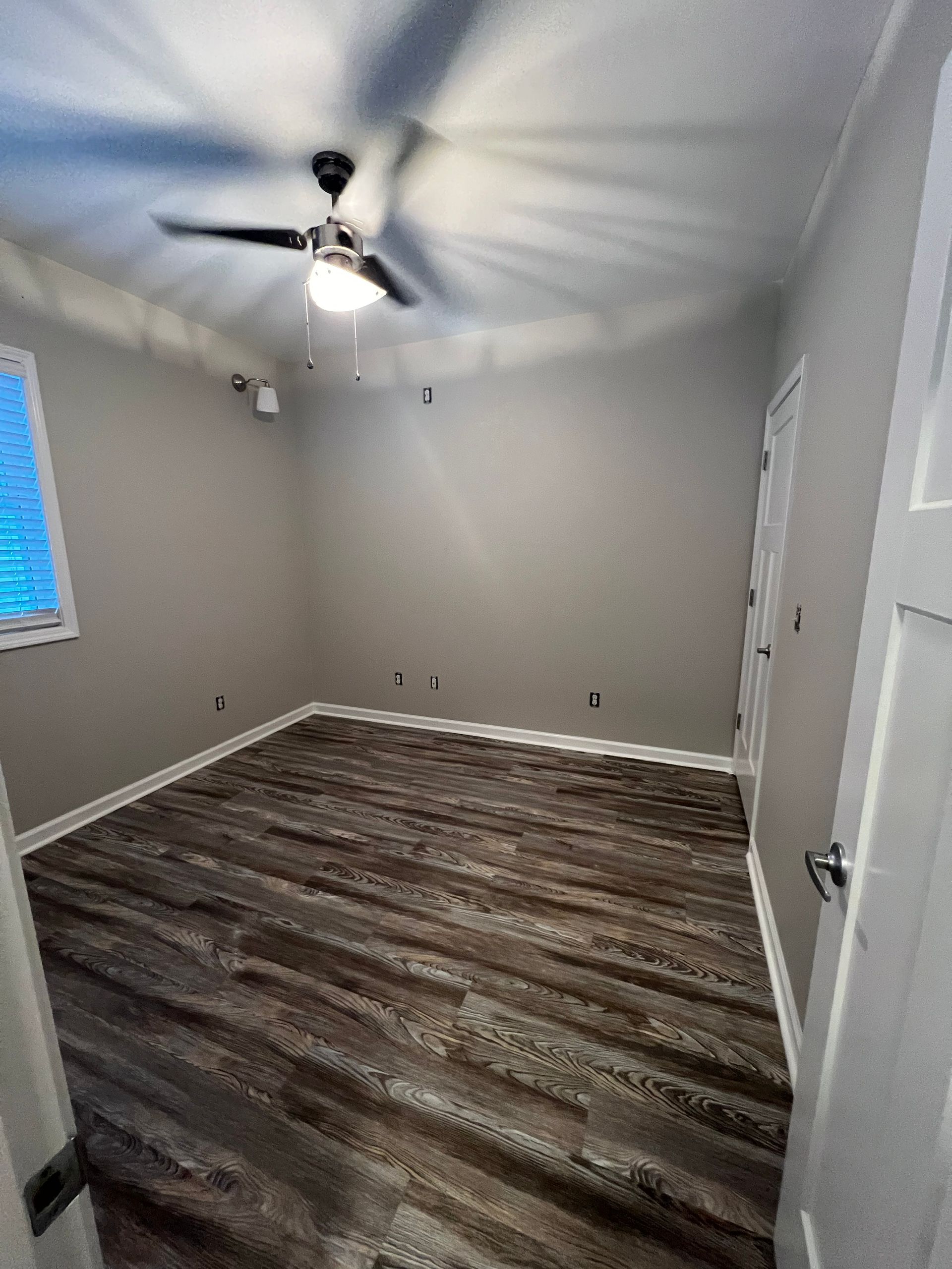 Empty room with gray walls, wood-look floor, ceiling fan, and window.