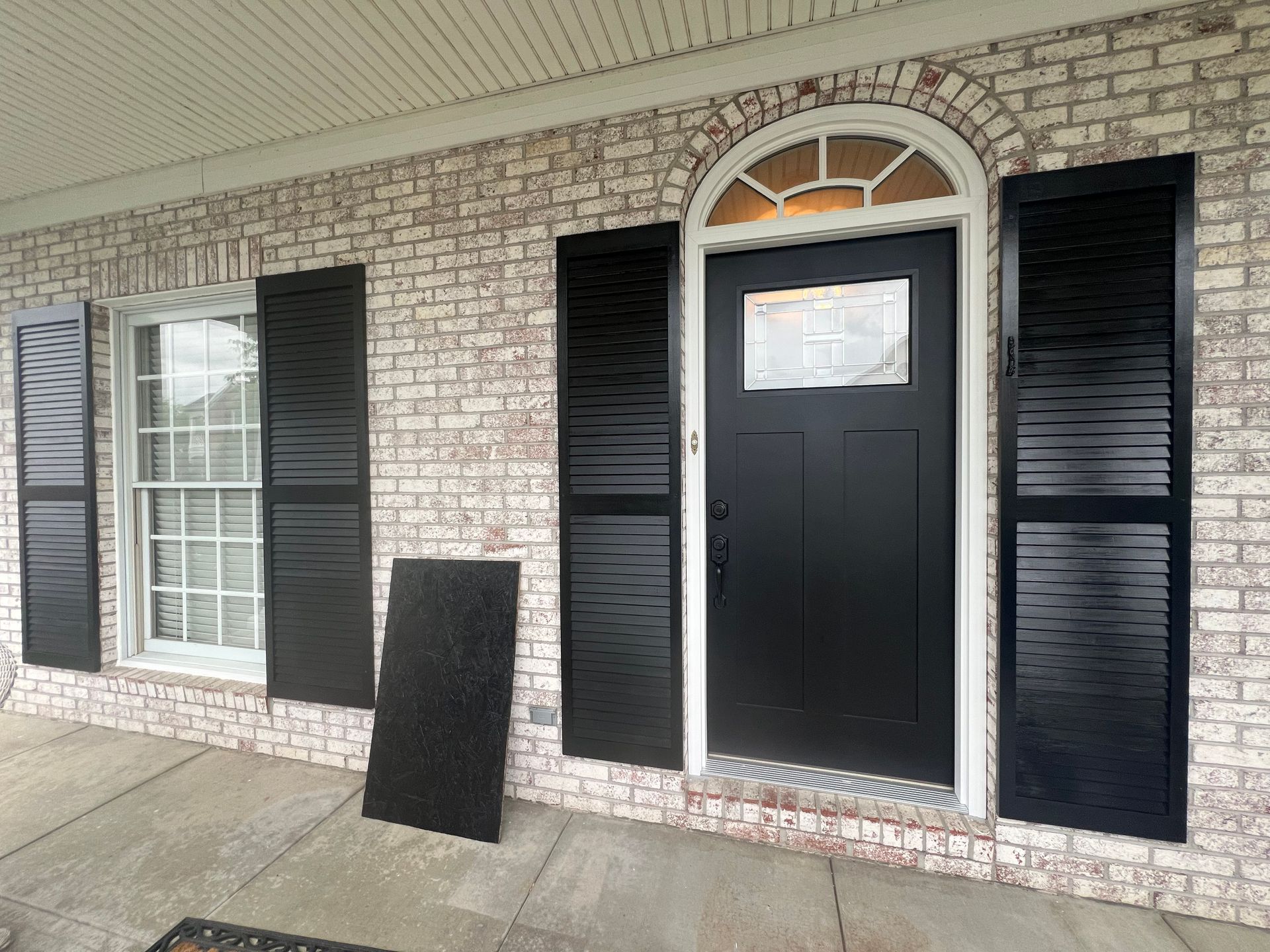 Black door and shutters on a white brick building. A black ramp leans against the wall.
