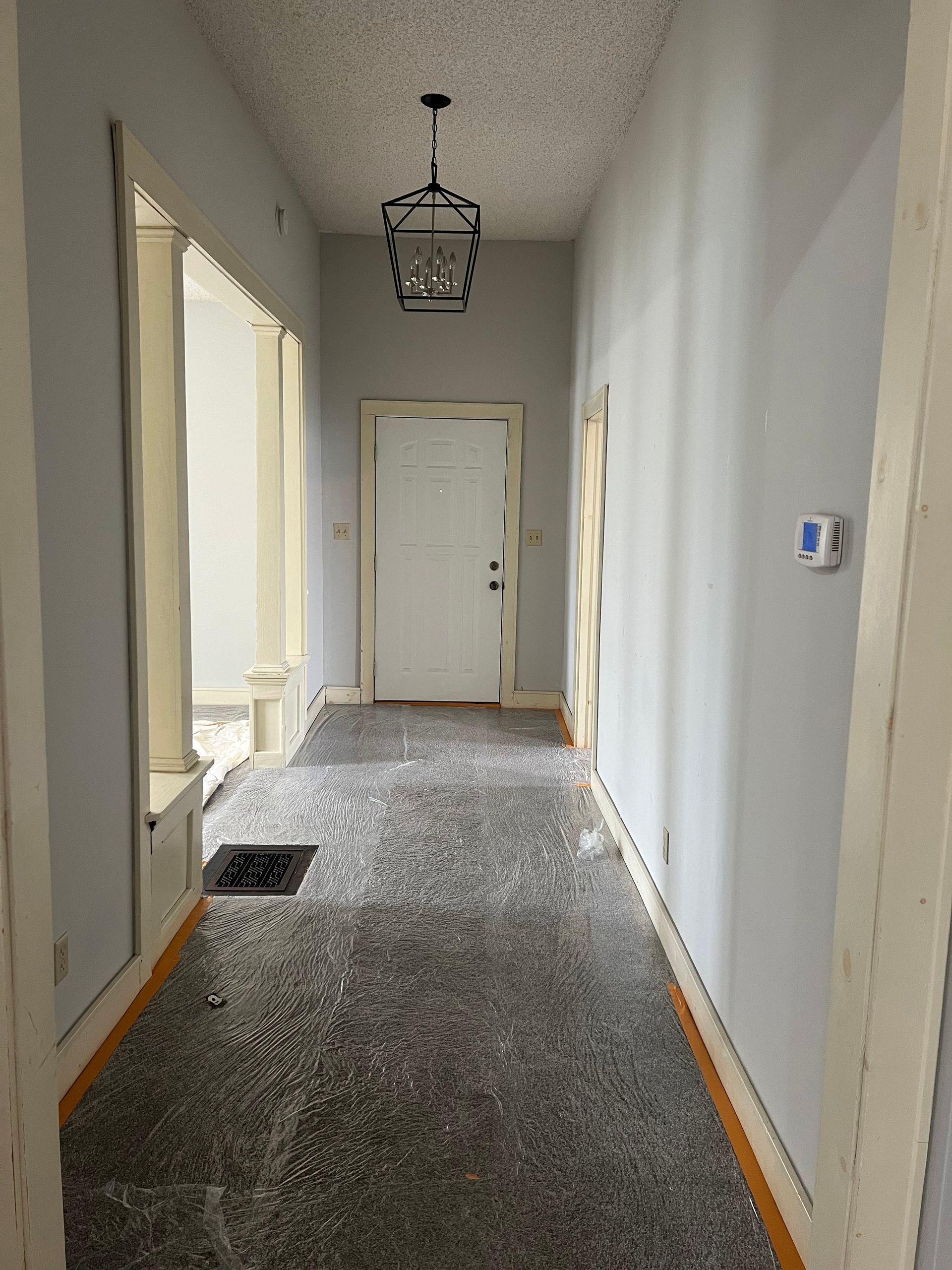 Long hallway with pale blue walls, white door, decorative light fixture, and speckled floor.