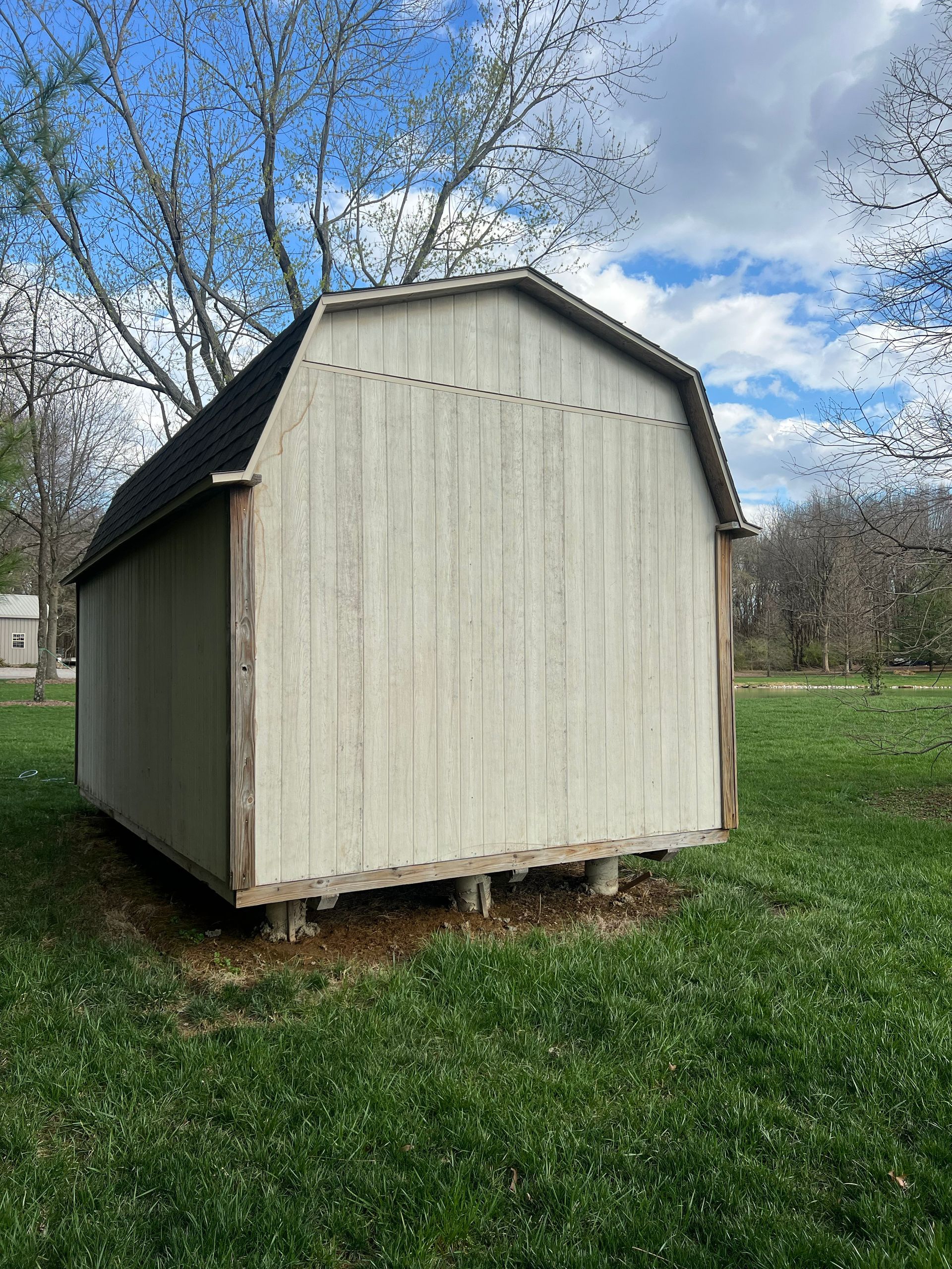 Tan barn shed in a grassy yard under a cloudy blue sky.