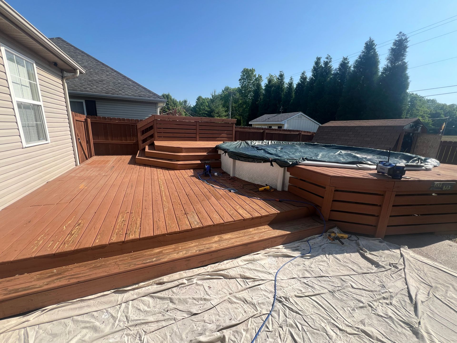 Wooden deck painted brown with steps leading to an above-ground pool, sunny day.