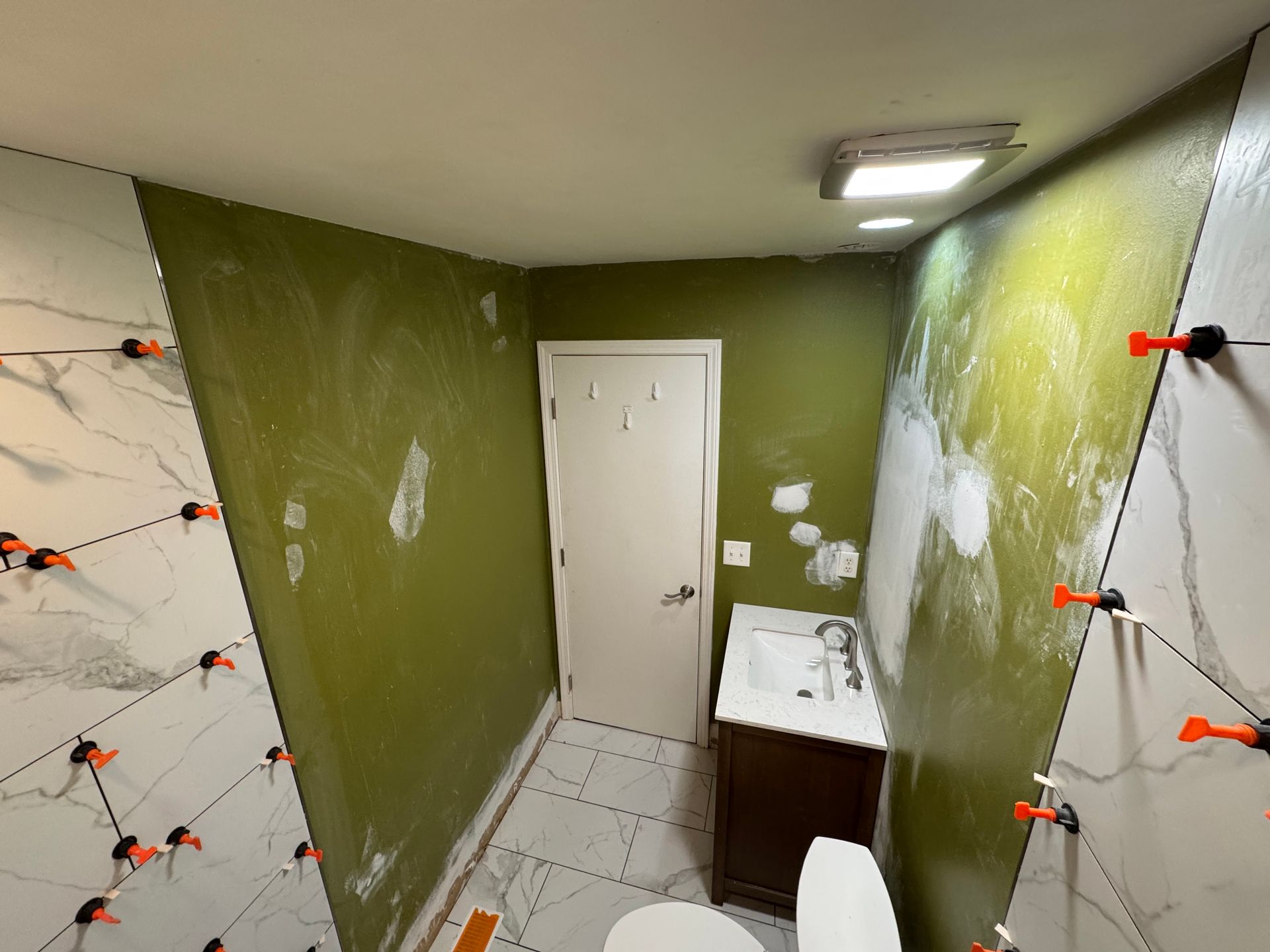 Bathroom under renovation with green walls, marble-look tile, and a toilet.
