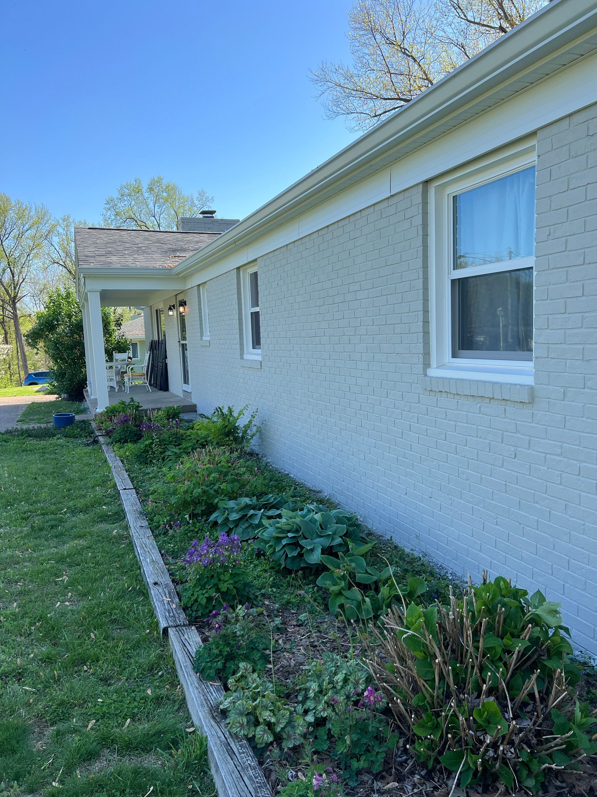 Light gray house with a flower bed in front, on a sunny day.