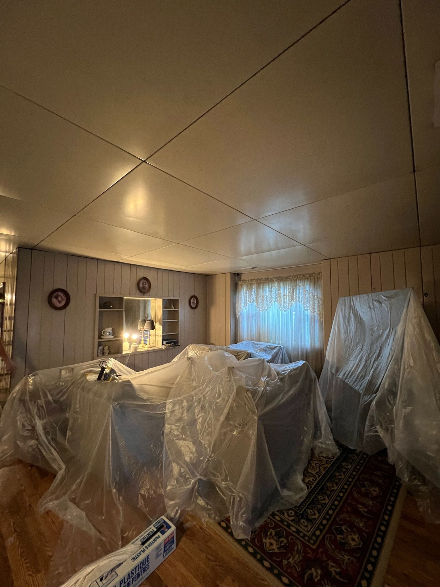 Living room covered in plastic for painting. Furniture and floor protected, light-colored walls.