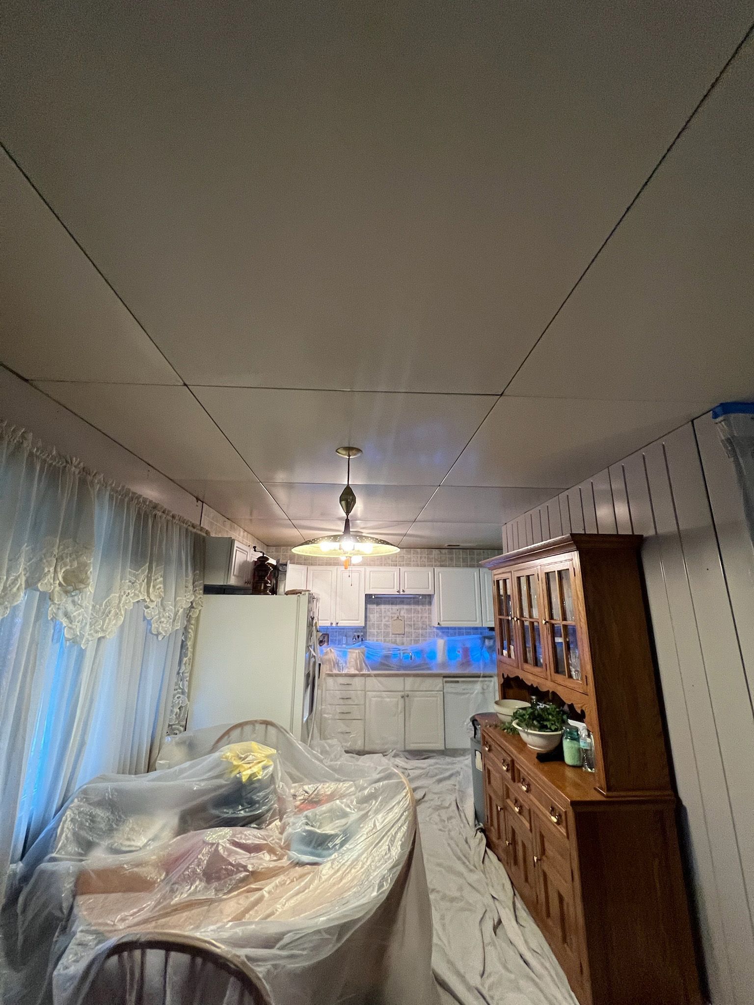 Room being renovated; kitchen visible in the background. Furniture and table covered in plastic sheeting.