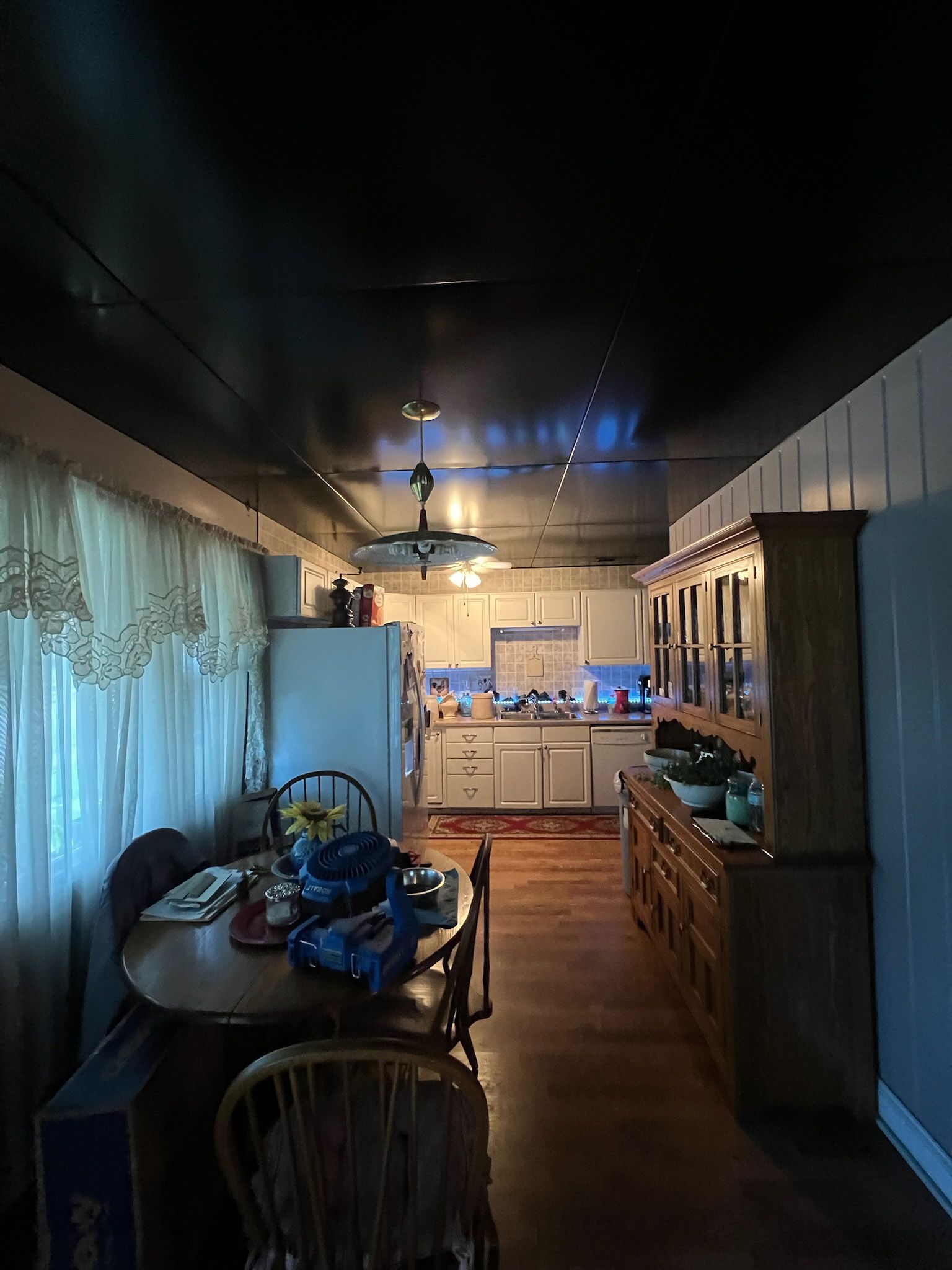 Dark kitchen with table, chairs, refrigerator, cabinets, and a hutch.