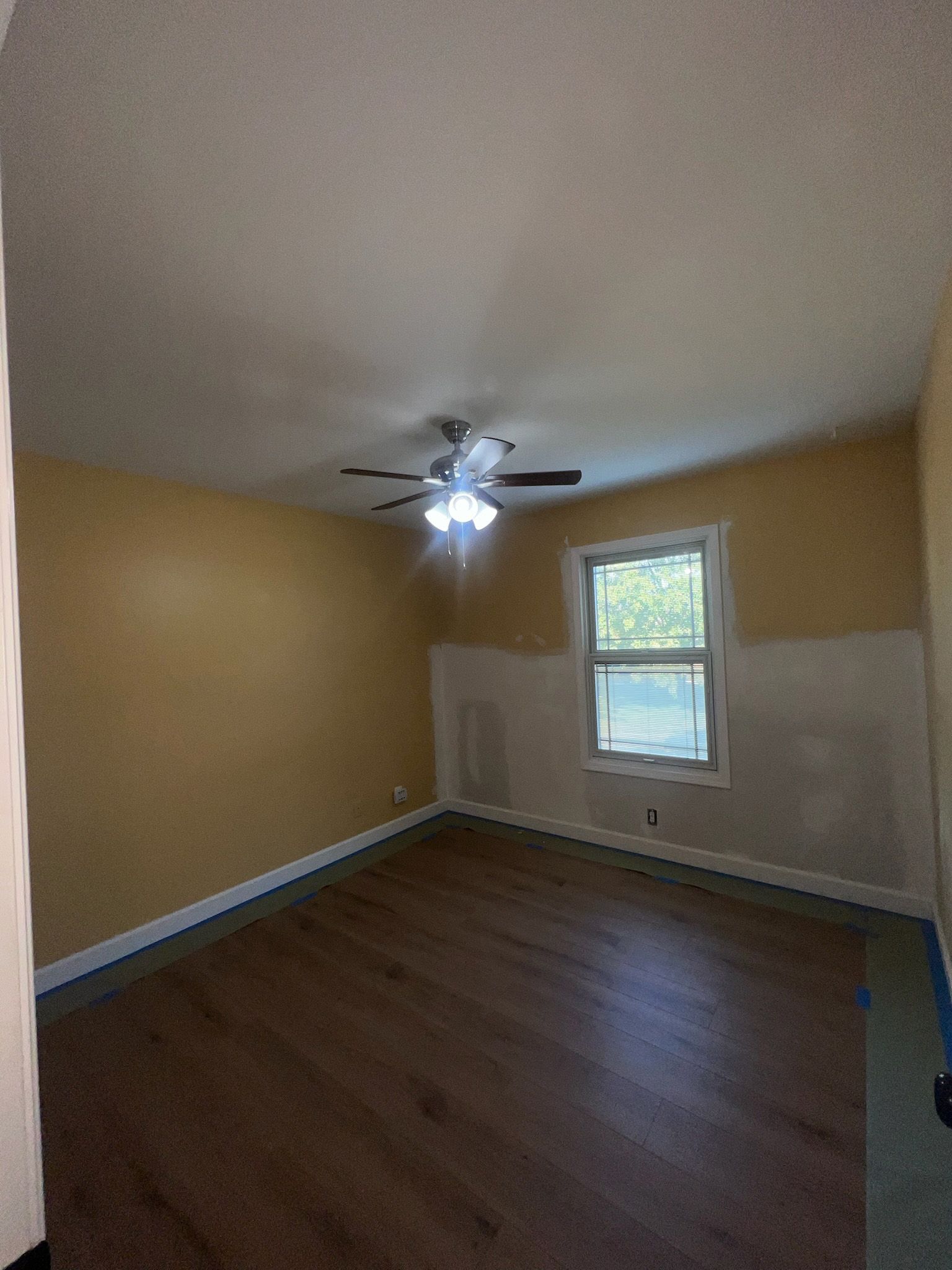 Empty room with wood flooring, yellow walls, ceiling fan, and a window.