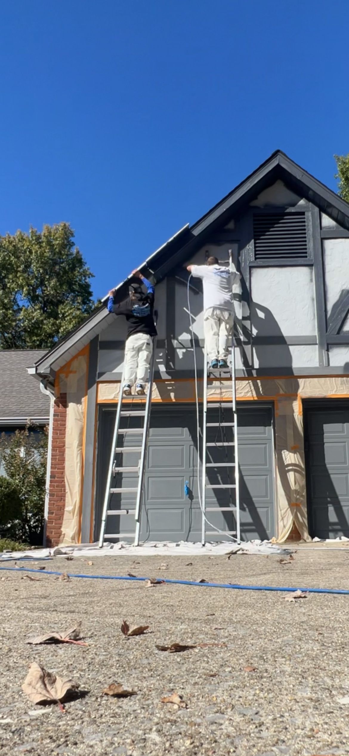 Two workers painting the exterior of a Tudor-style house; blue sky.