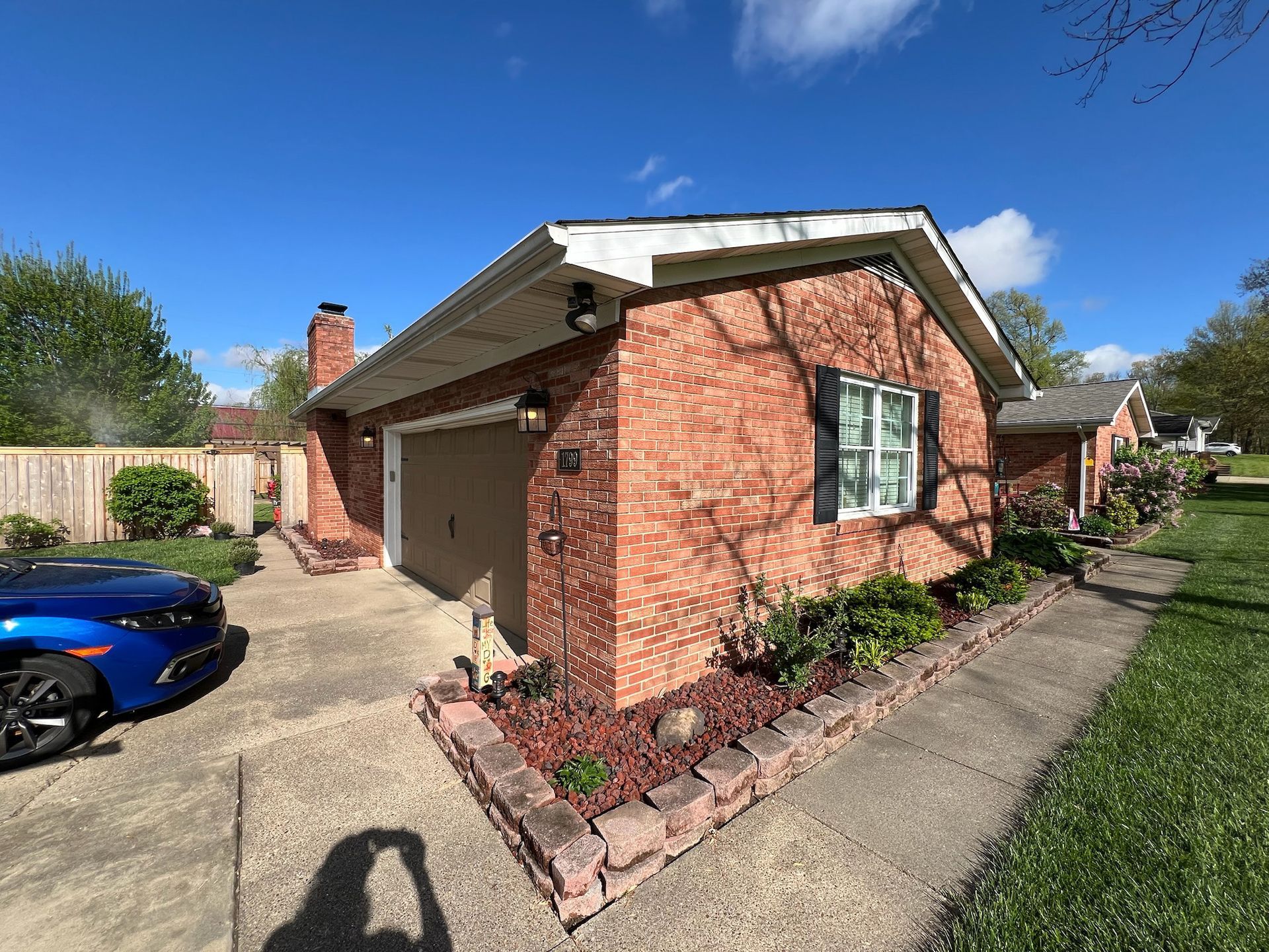 Brick house with a tan garage door and a blue car in the driveway on a sunny day.