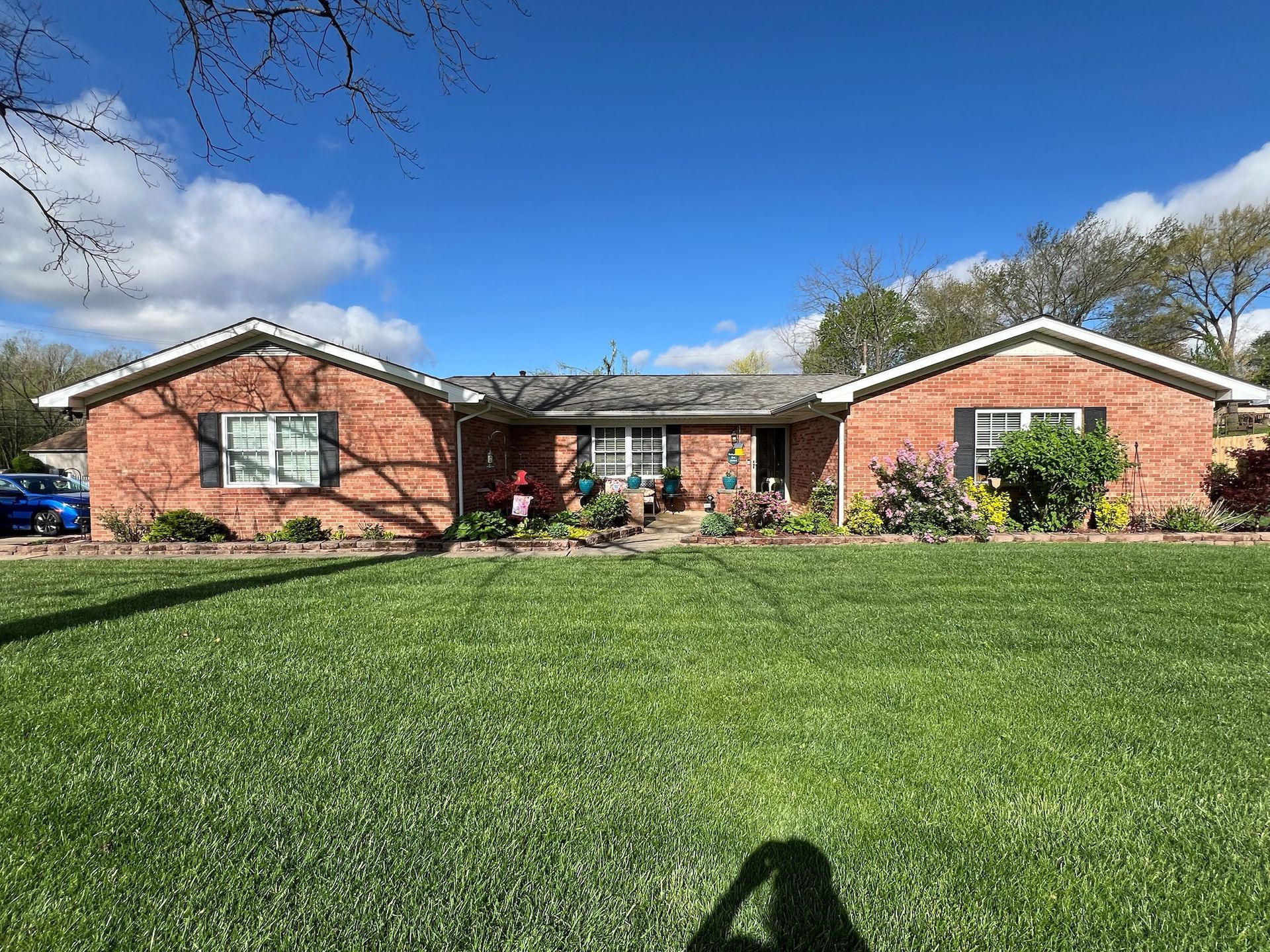 Red brick ranch-style house with green lawn, blue sky, and scattered clouds.