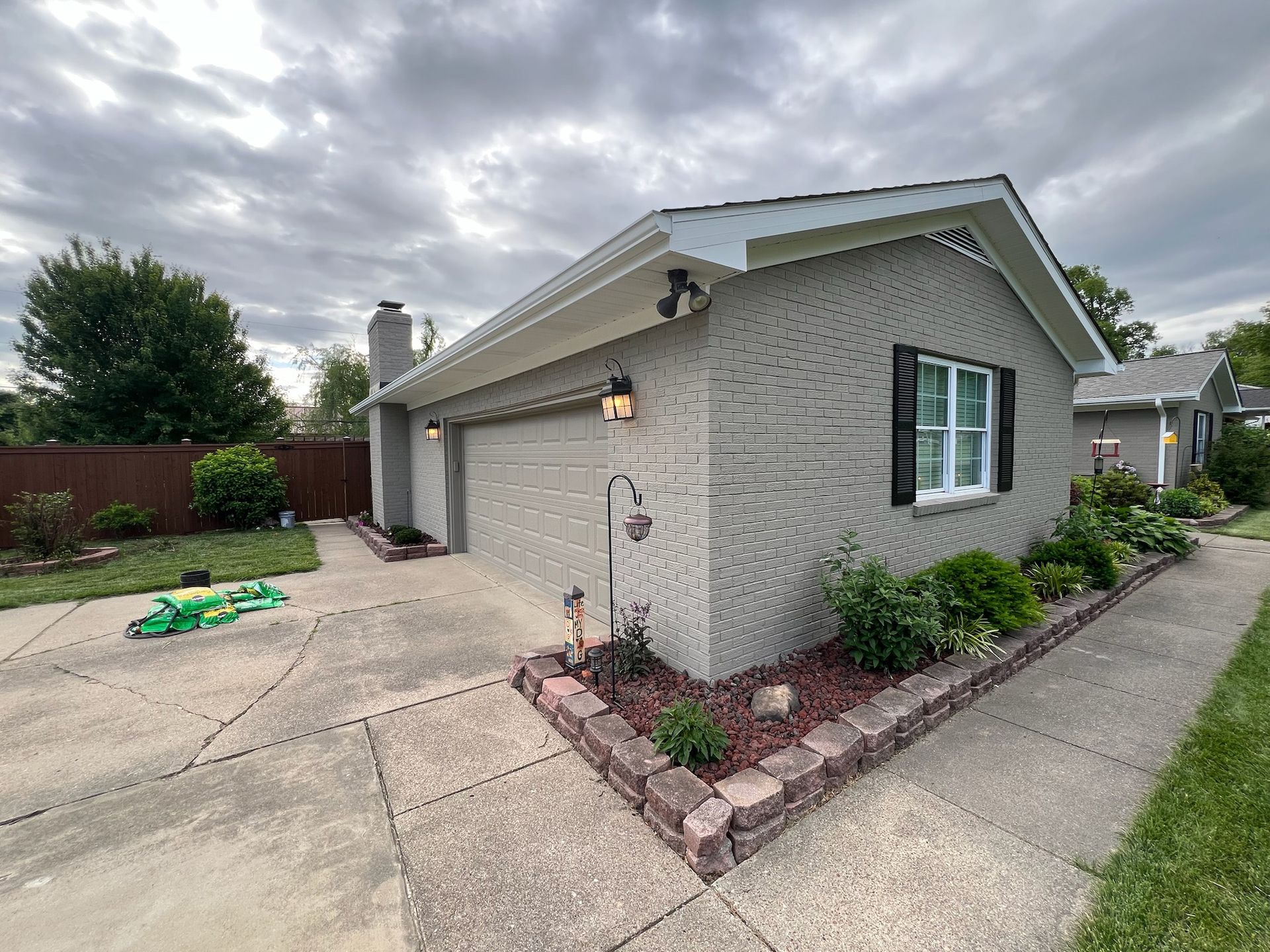 Gray brick house with a driveway, garden, and a cloudy sky.