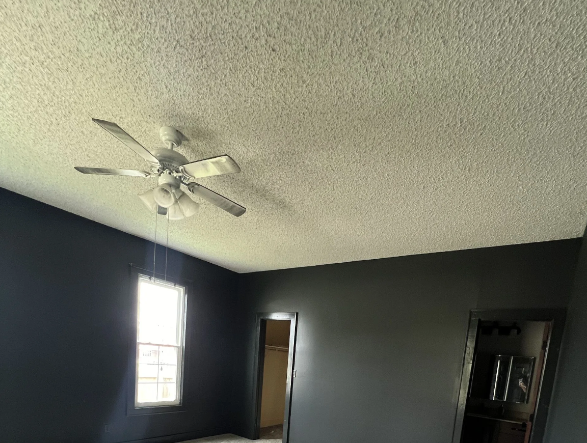 Dark gray room with a white textured ceiling, ceiling fan, and small window.