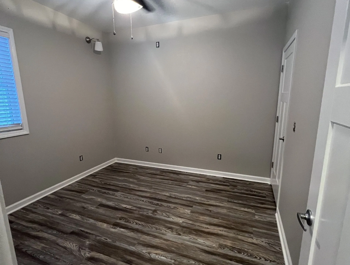 Empty room with gray walls, wood-look flooring, white trim, and closed white door.