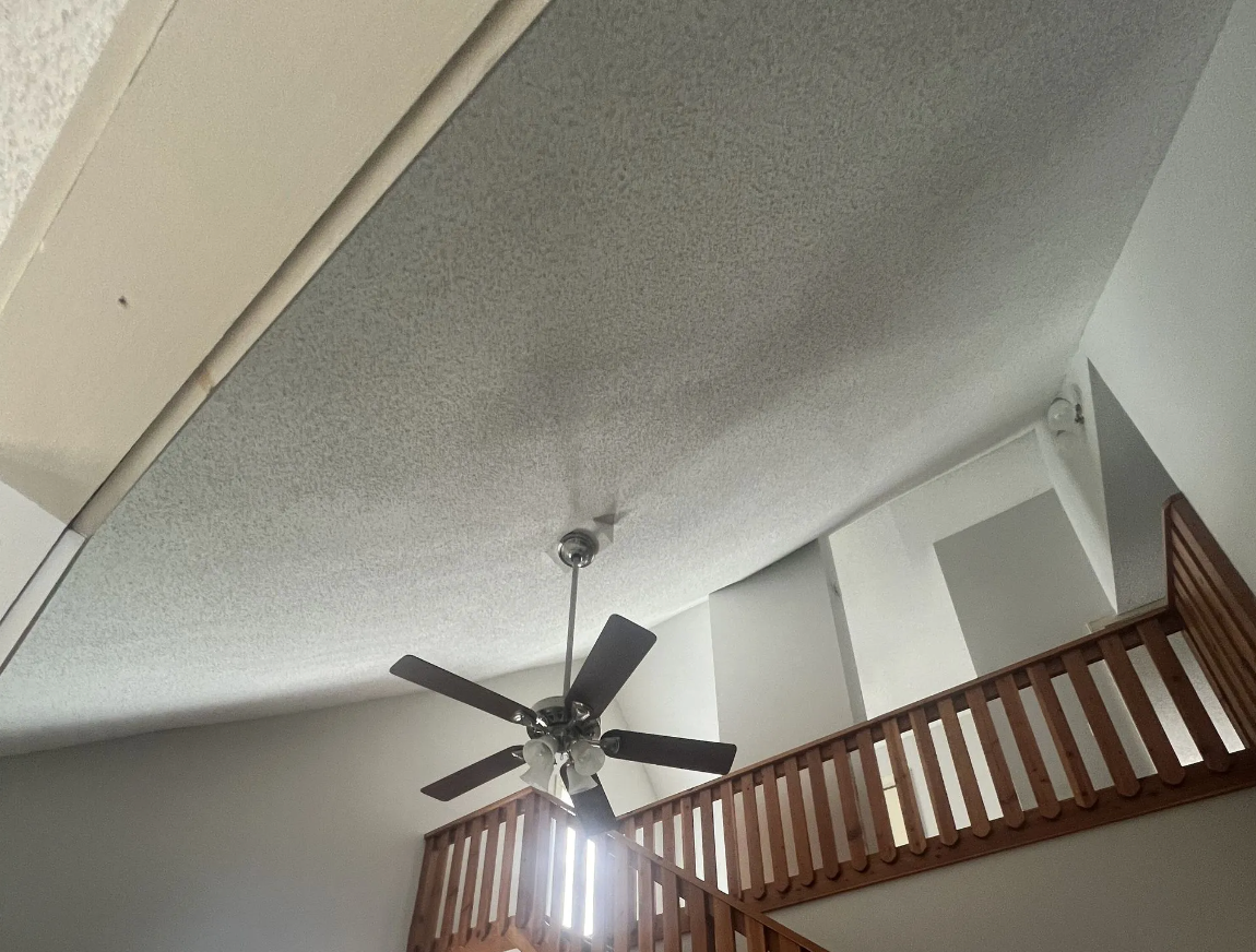 High-ceilinged room with a popcorn ceiling, a ceiling fan, and a wooden balcony.