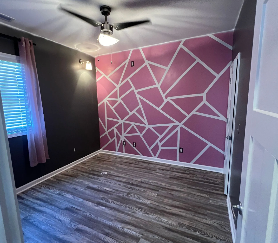 Bedroom with pink geometric accent wall, dark gray walls, and wood-look flooring.