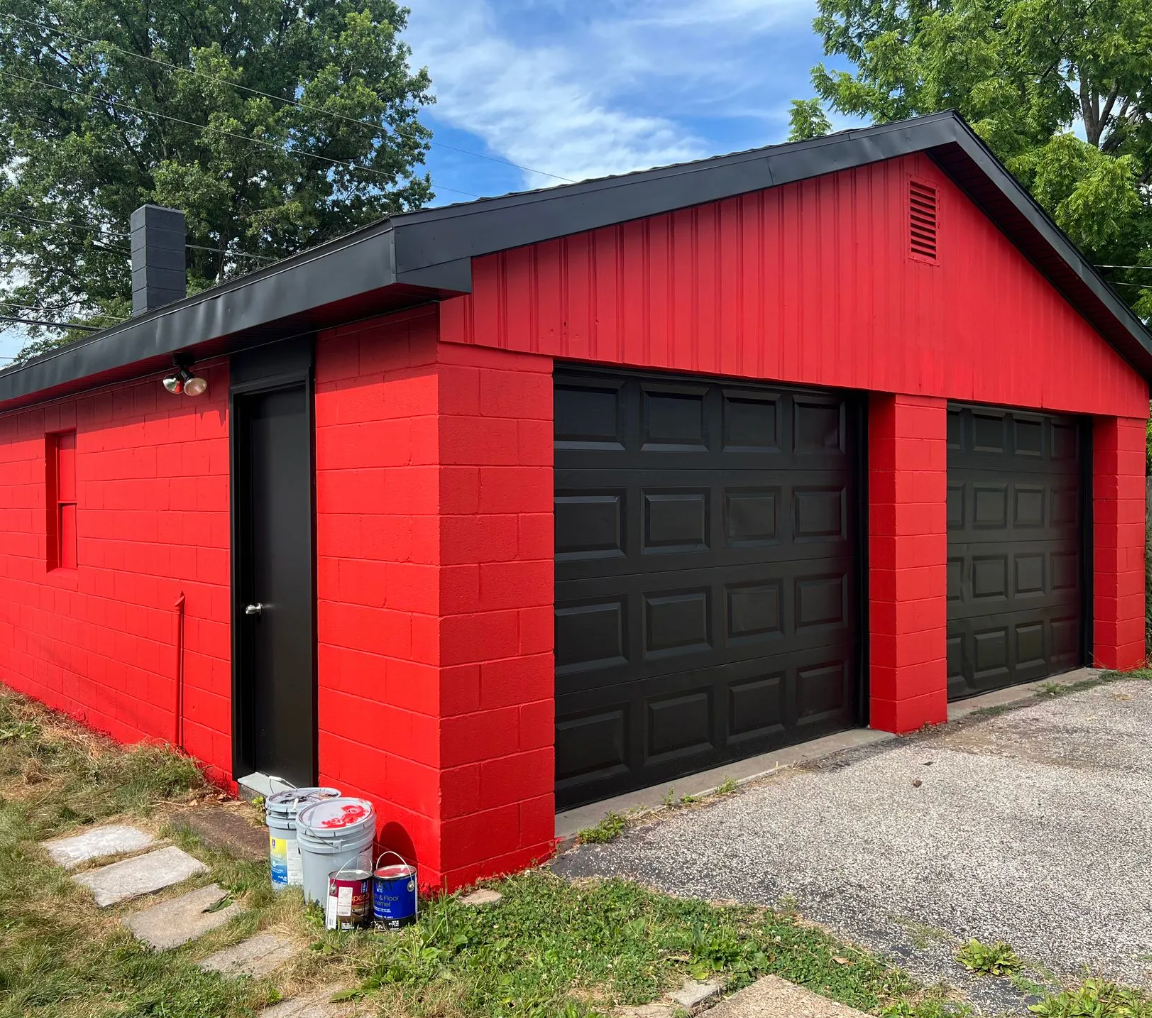 Red and black garage with two doors, a side door, and a chimney.