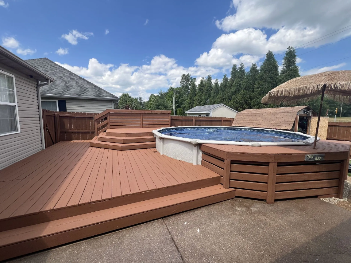 Brown deck with steps leading to an above-ground pool on a sunny day.
