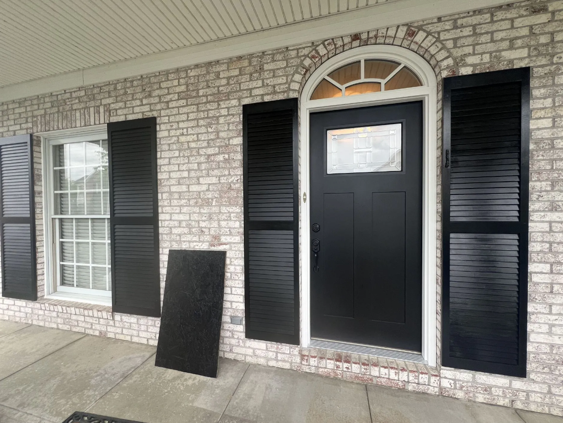 Exterior of a brick house with black shutters and door. White trim, porch.