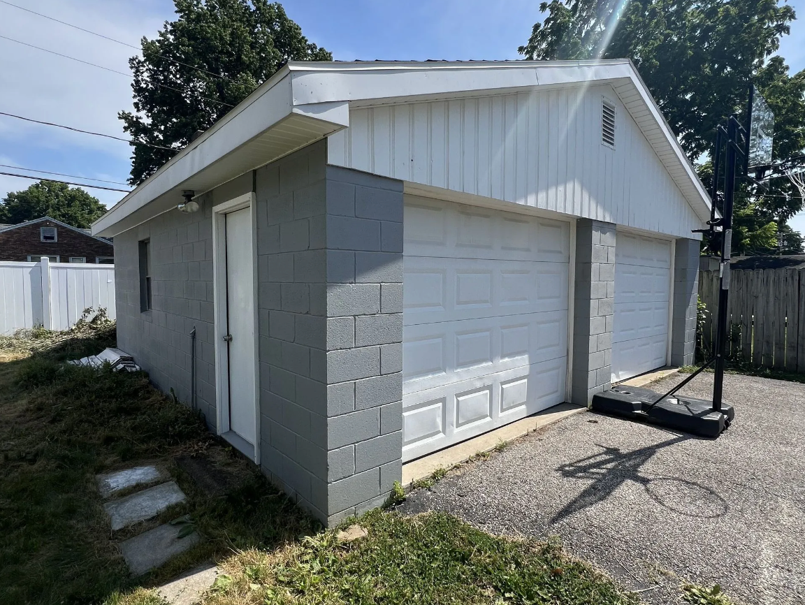 Gray two-car garage with white doors. A basketball hoop is on the right.