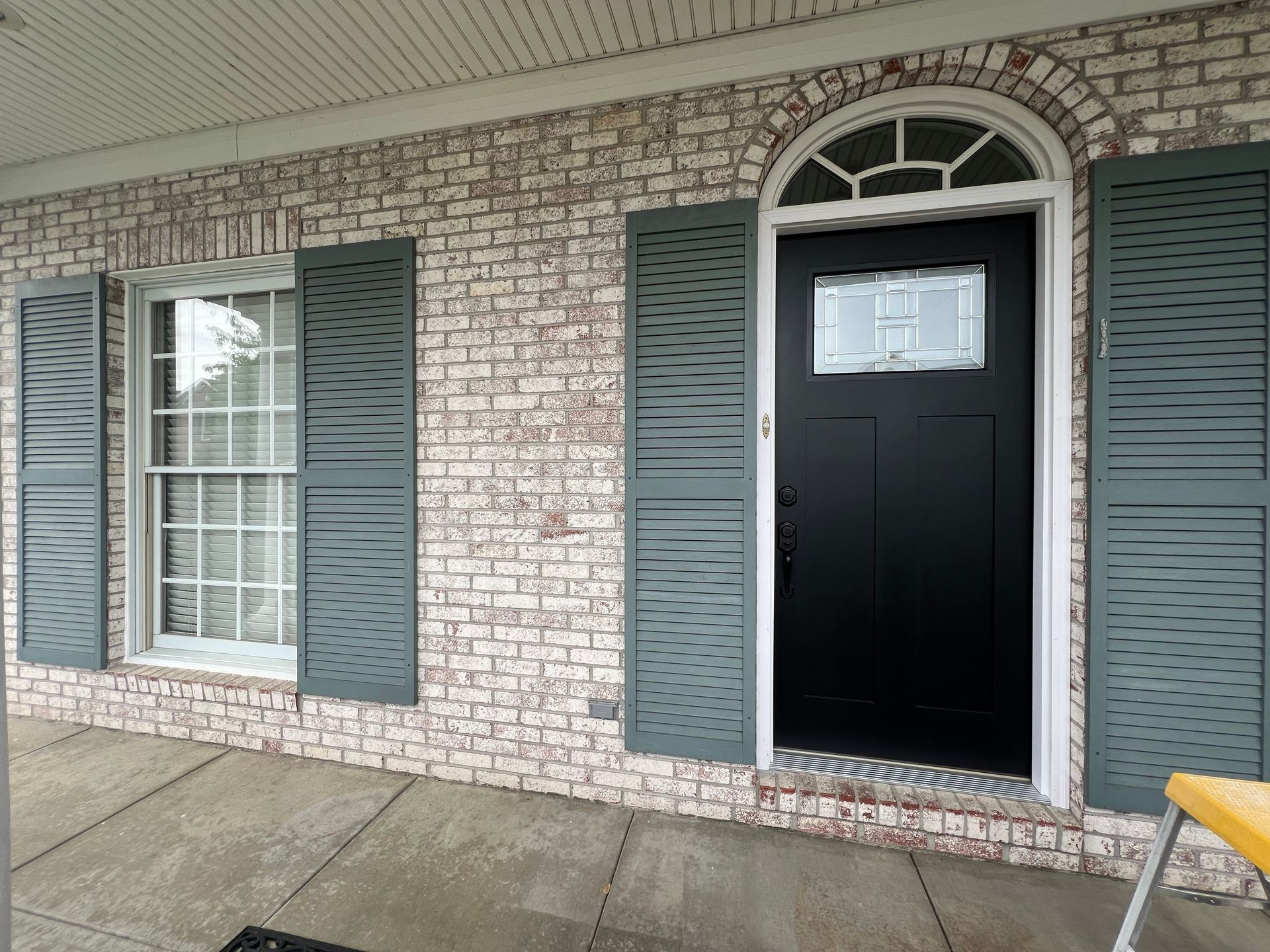 White brick exterior with teal shutters and a black front door under an arched window.