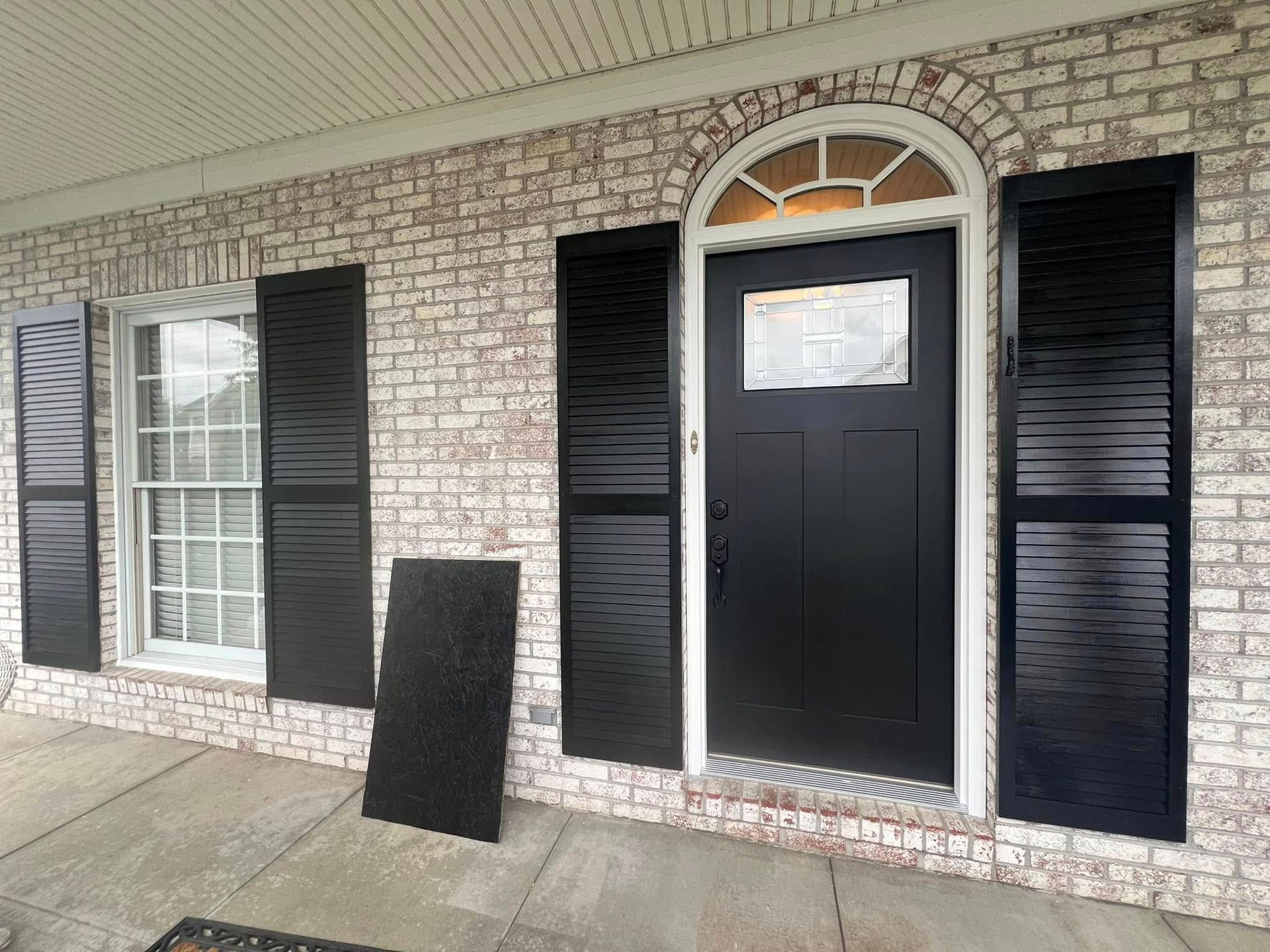 Exterior of a house with black shutters and door against a brick wall. A black ramp sits on the concrete.