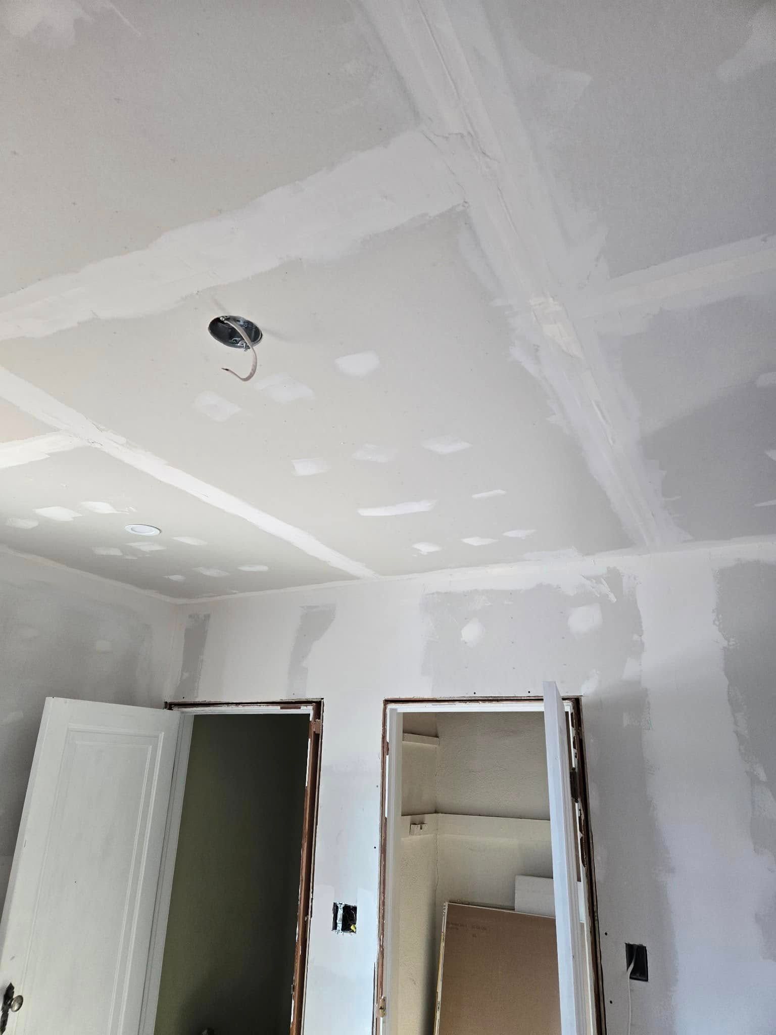 Drywalled ceiling with exposed electrical box, doorways, and partially finished walls.
