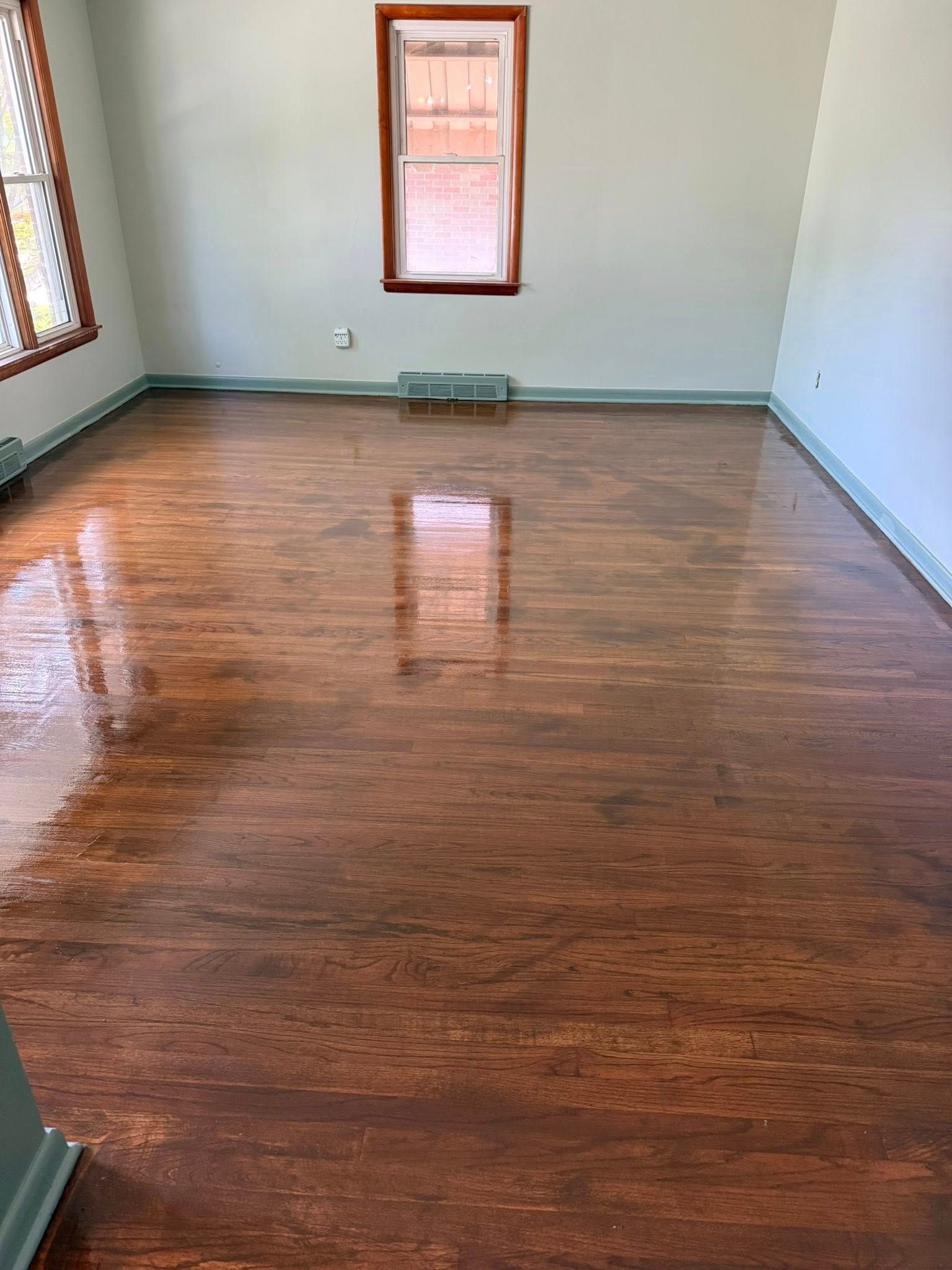 Room with polished, dark wood floors, light green walls, and a small window reflecting light.