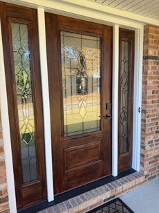 Brown wooden front door with stained glass windows, framed by white trim and brick.