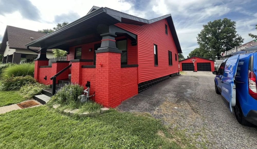 Red house with black trim, porch, and garage on a gravel driveway, blue van parked nearby.