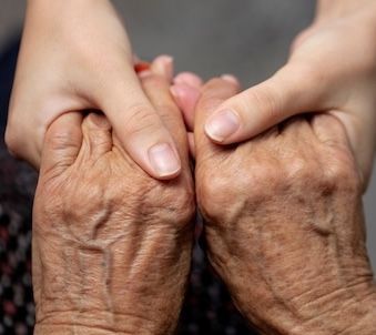 Young hands gently holding the wrinkled hands of an older person, offering support.