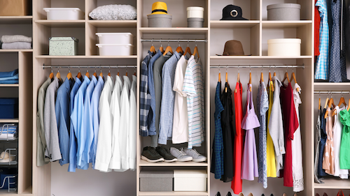 Organized closet with hanging clothes in various colors and shelves holding boxes and hats.